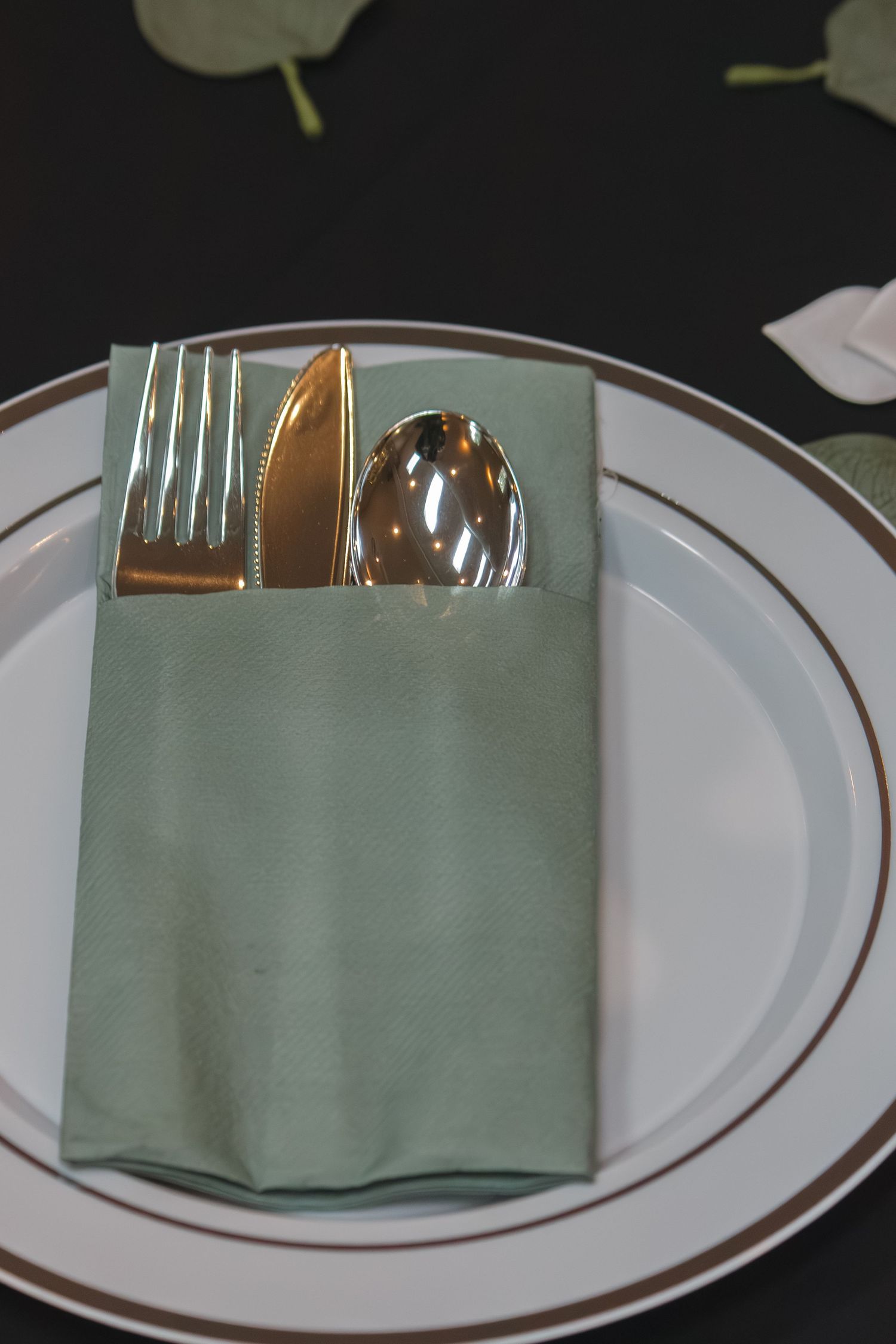 White dinner plate with sage green napkin and silver cutlery arranged formally.