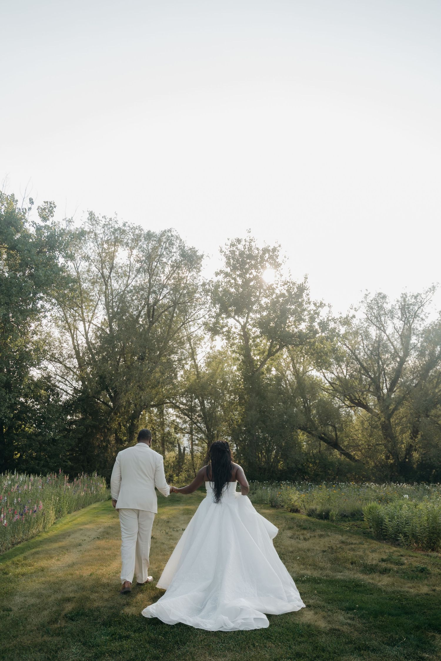 Bride and groom holding hands walking through lush green gardens in golden hour light, bride in flowing white ballgown.