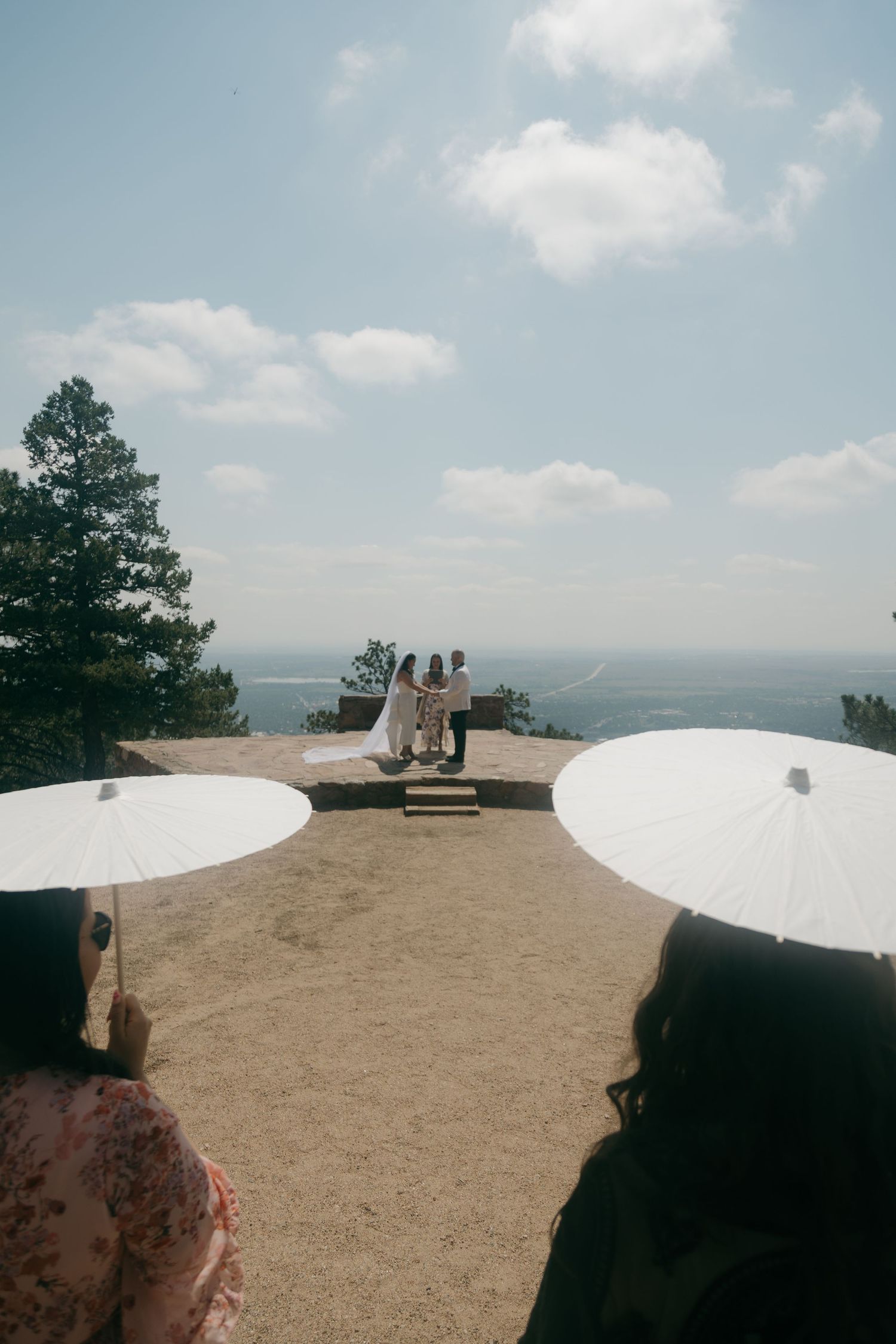 Outdoor wedding ceremony on mountain overlook with guests holding white parasols.
