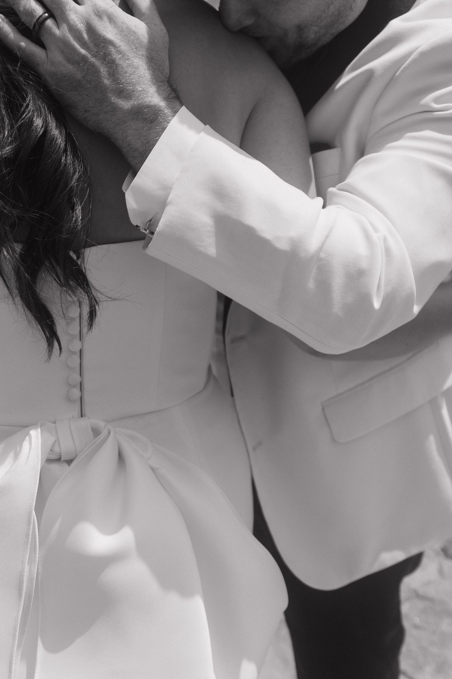 Black and white close-up of a groom in a white jacket embracing a bride in a white dress, showing tender affection.