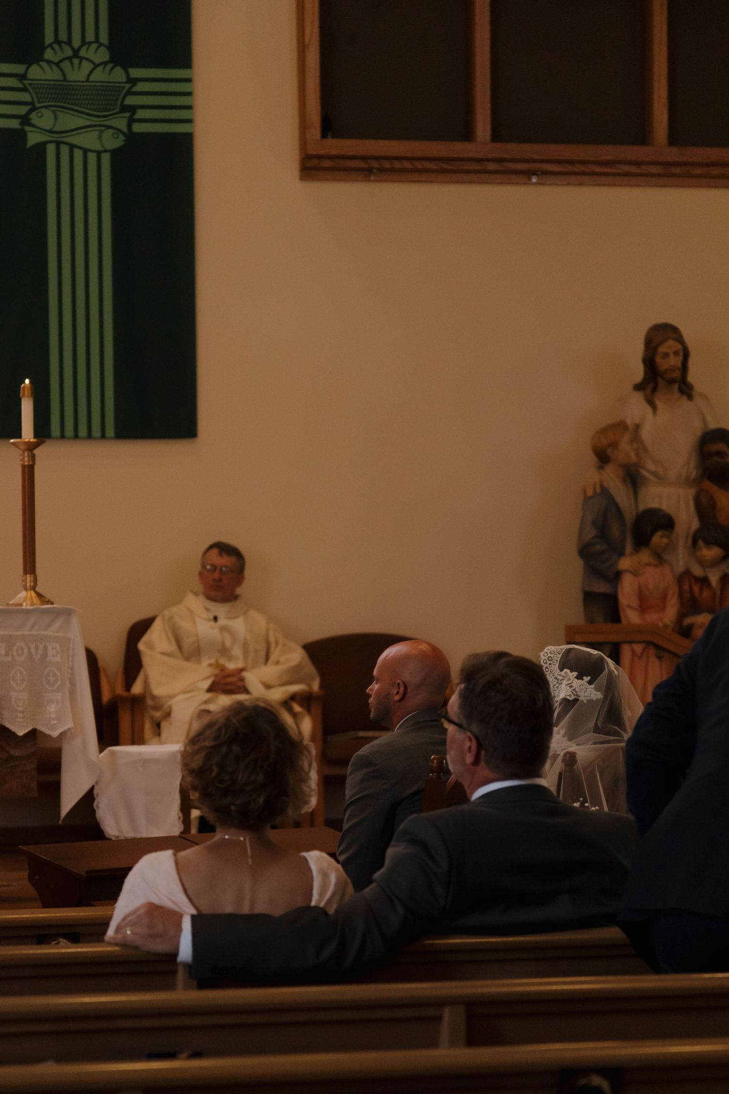 Wedding guests seated in church pews watching a priest during a Catholic wedding ceremony.