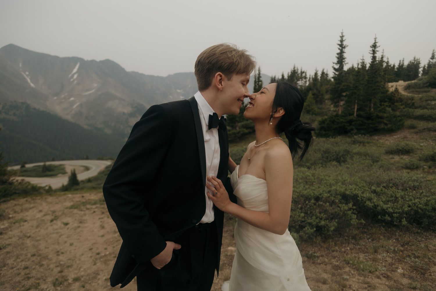 Happy couple in wedding attire share an intimate moment with misty mountain lake views behind them.