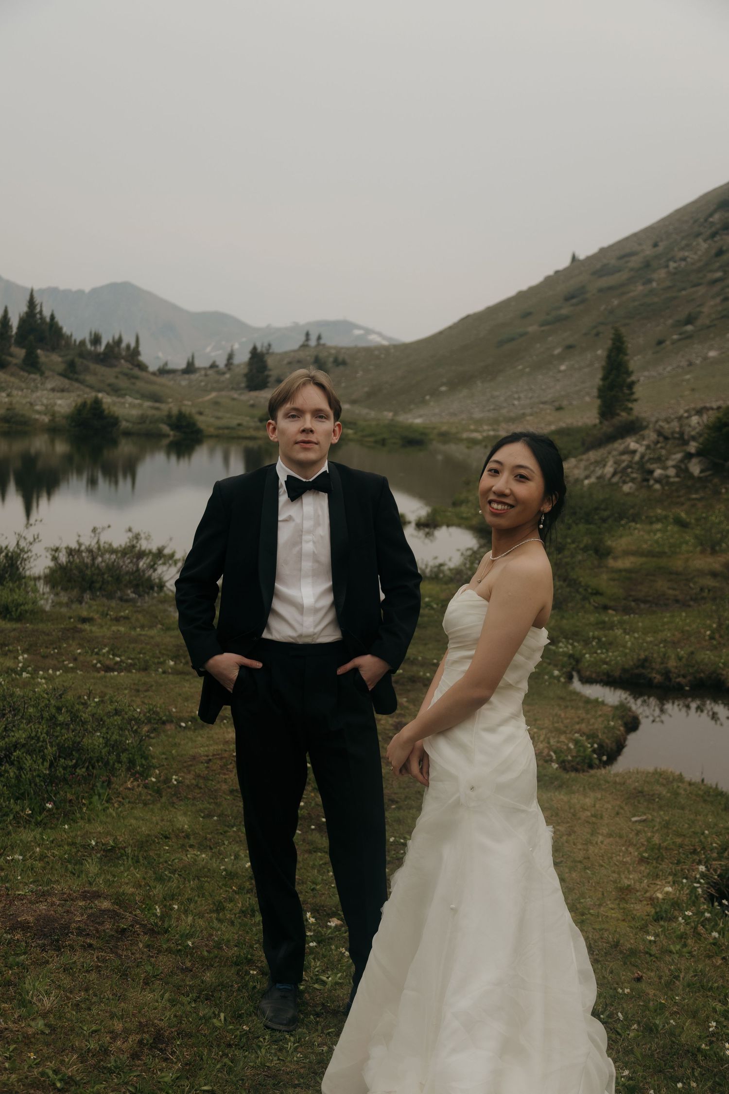 Bride and groom pose together smiling beside a serene alpine lake during their mountain elopement.