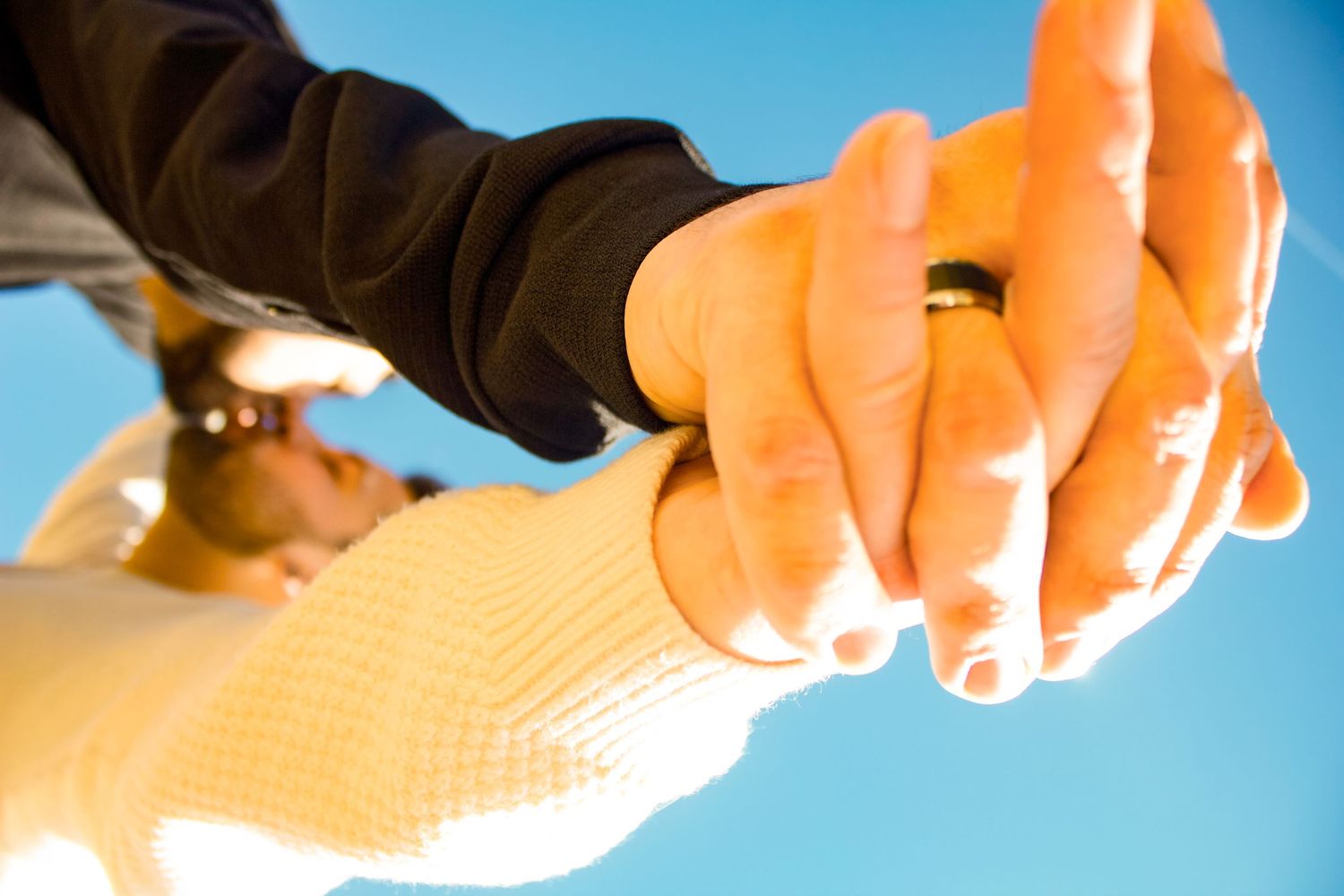Close-up of two hands clasped together against bright sky.