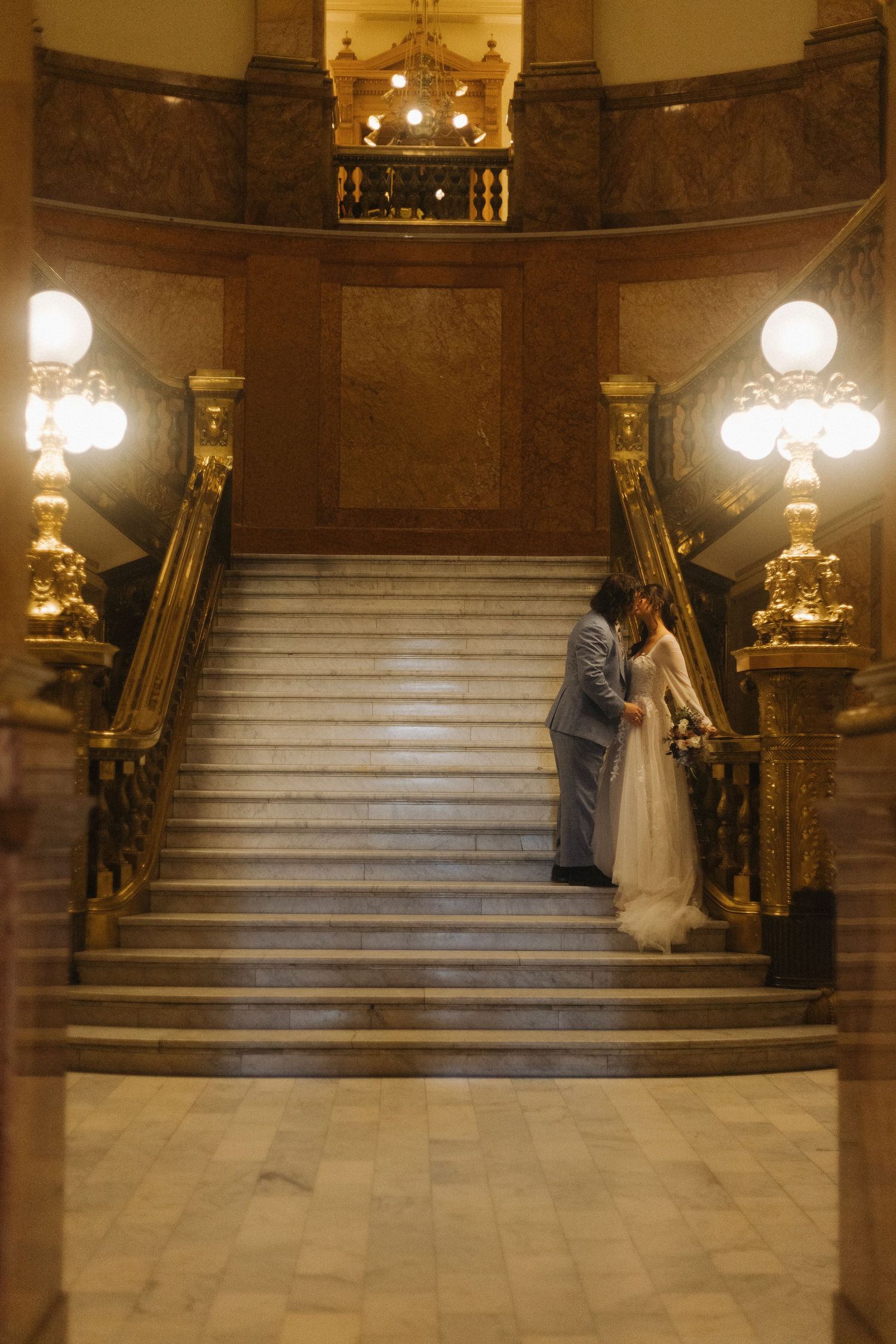 A grand marble staircase illuminated by ornate wall sconces creates an elegant wedding ceremony setting.