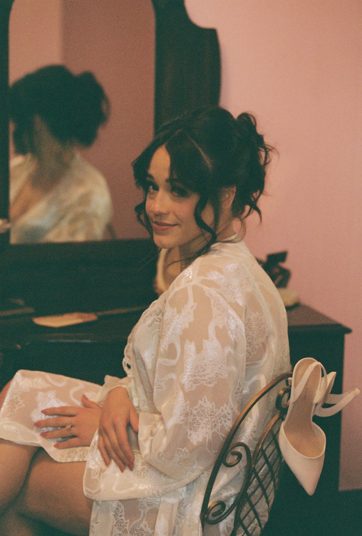 A person wearing a delicate white lace robe sits in a dimly lit room with warm lighting.