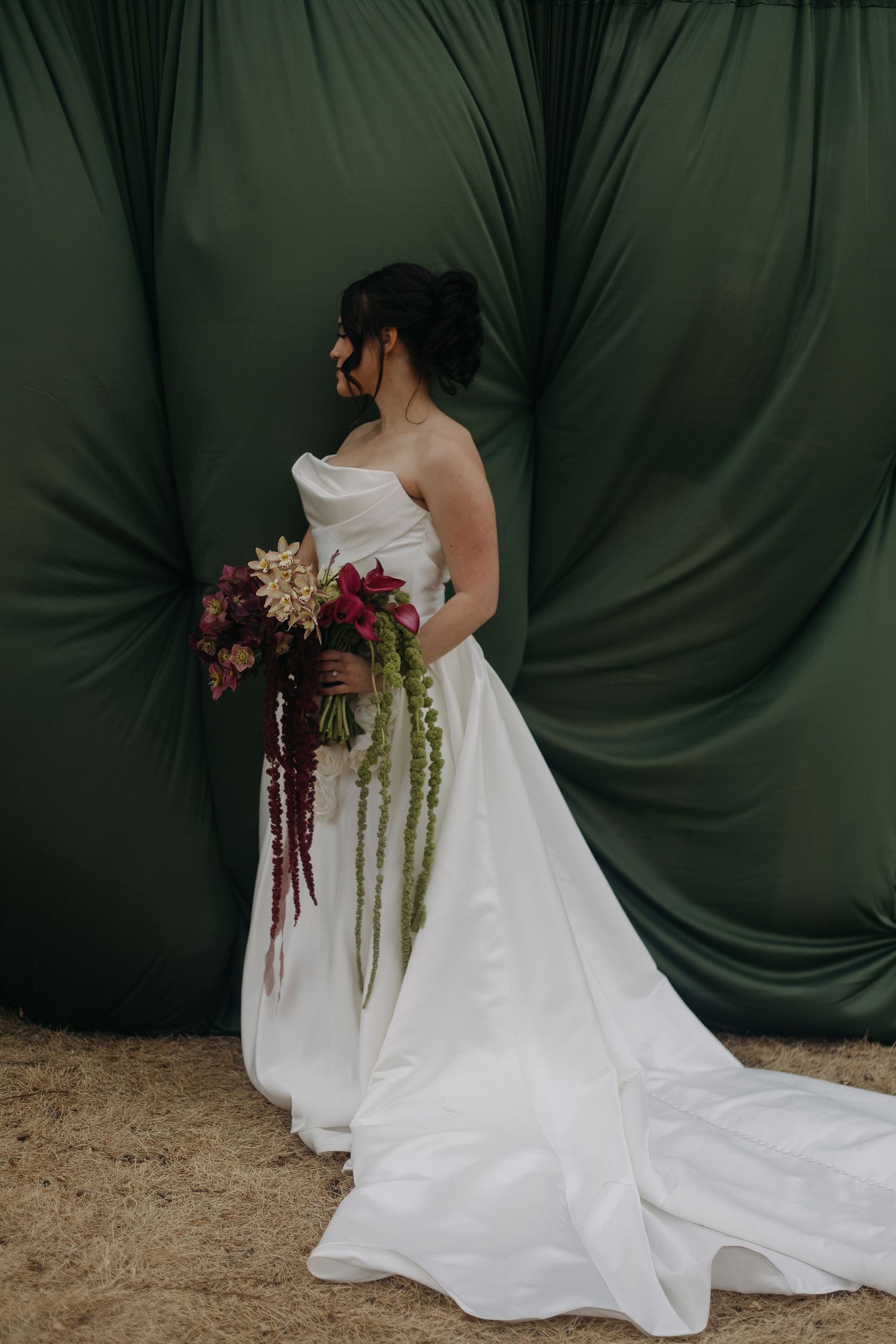 Dramatic bridal portrait against dark backdrop featuring flowing white gown and trailing bouquet.