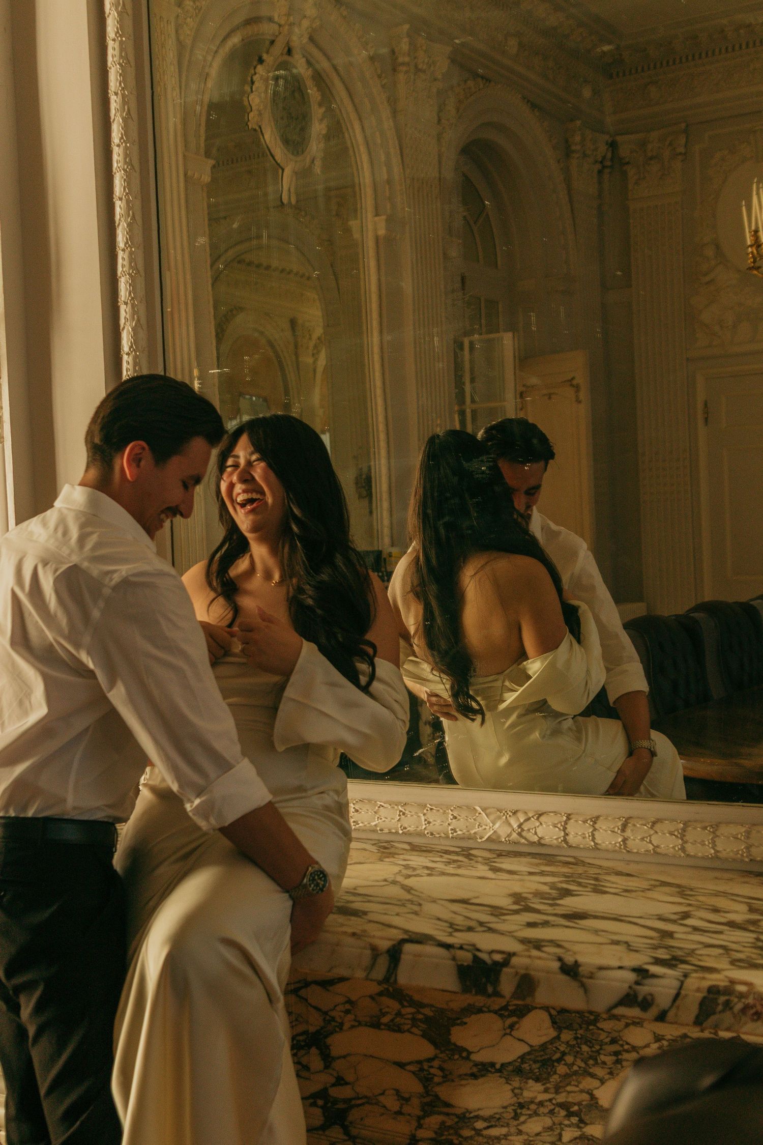 An intimate couple shares a playful moment in an elegant room with marble details and mirrors.