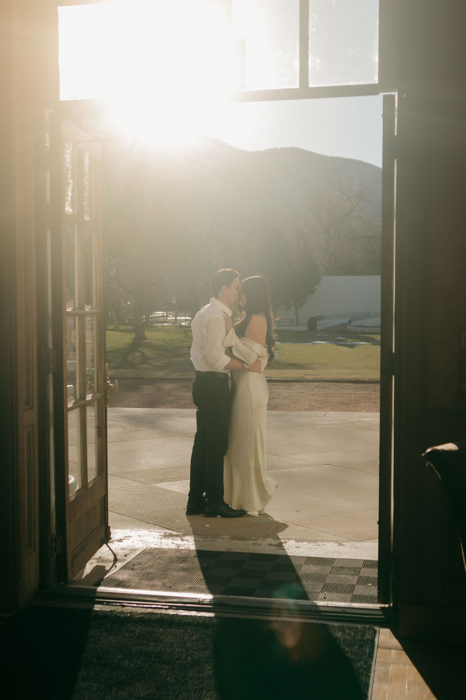 Silhouetted couple embracing in doorway during golden hour with mountain landscape in background.