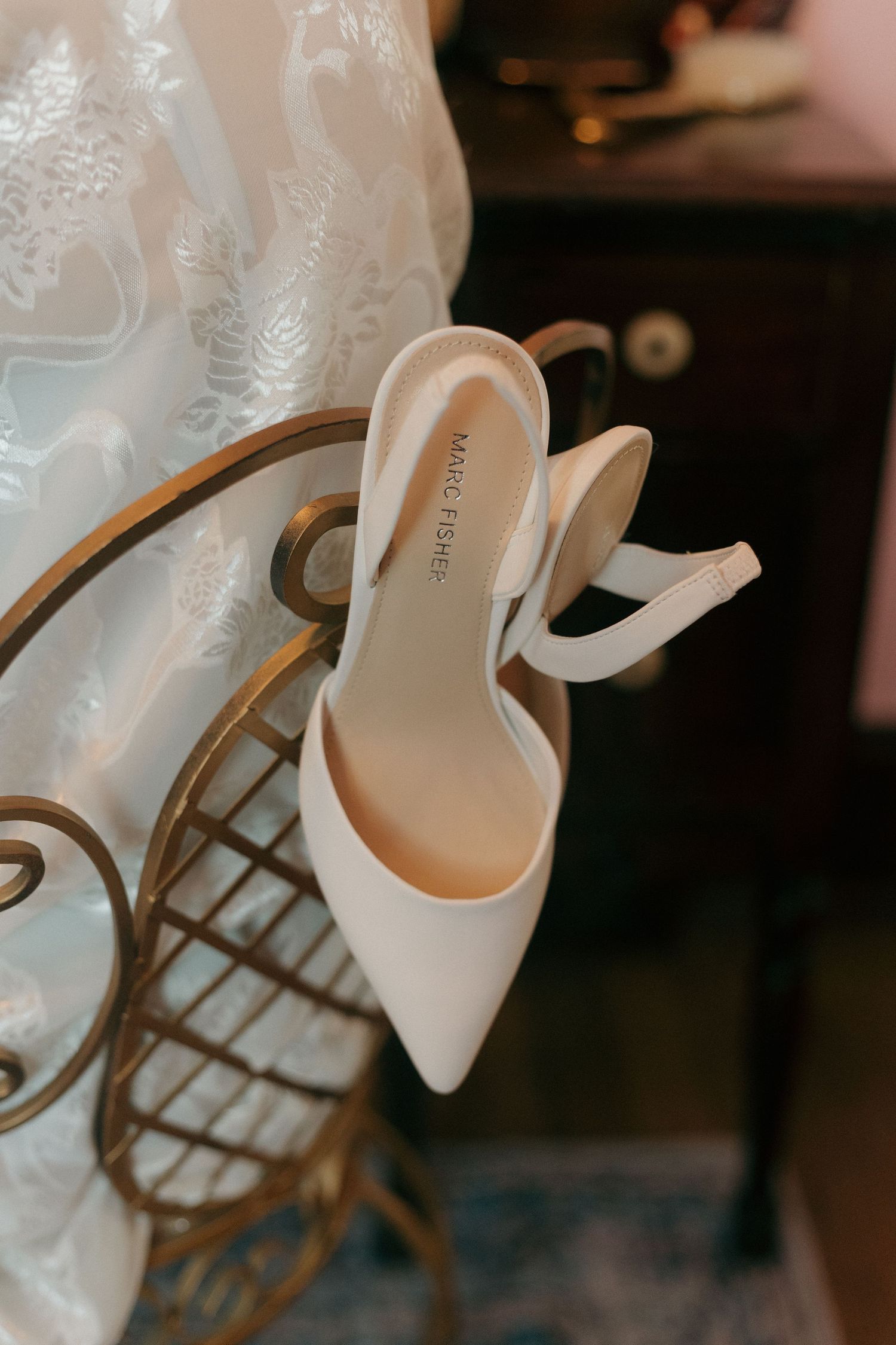 Elegant white bridal heels displayed against a textured lace background.