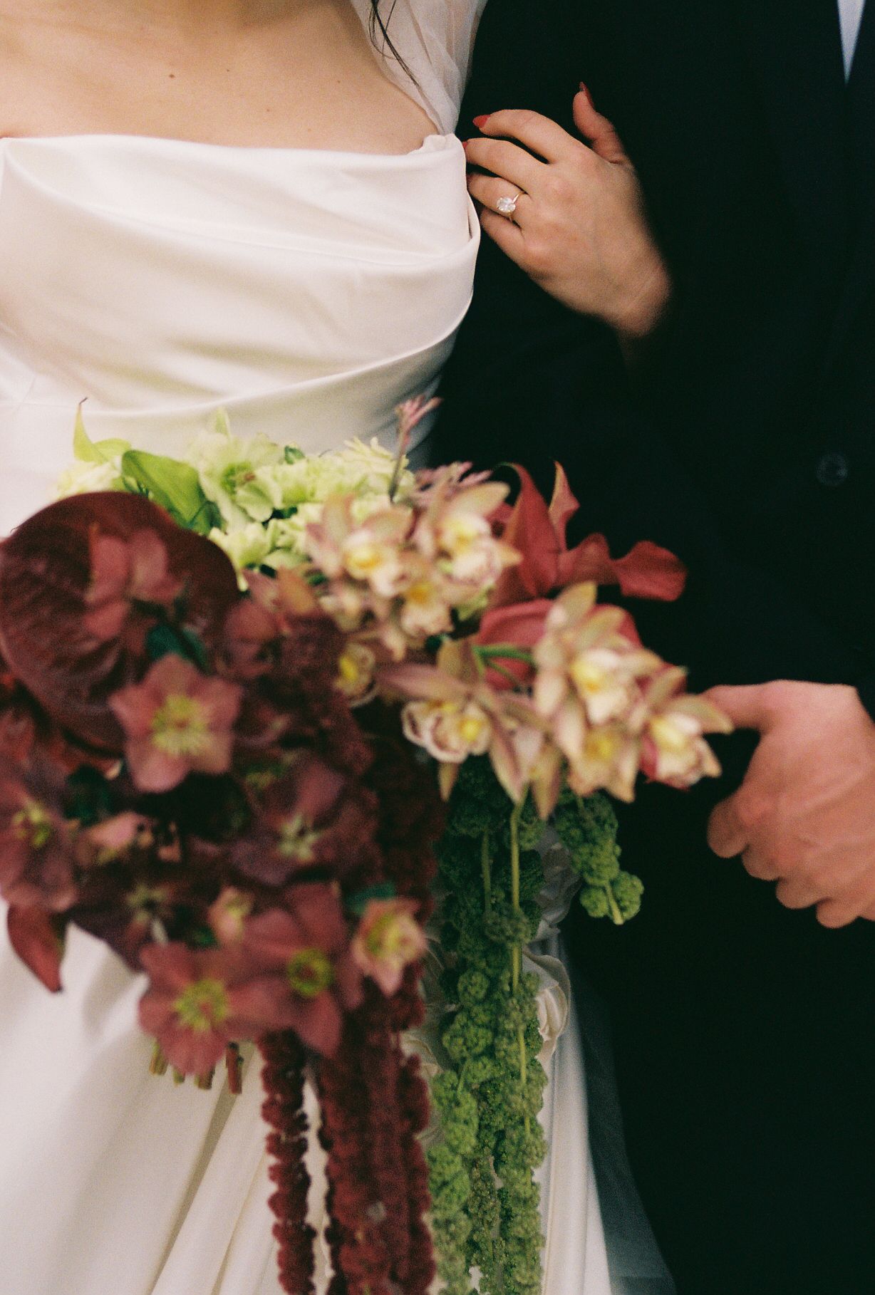 Close-up of a wedding bouquet with cascading burgundy and green florals against a dark background.