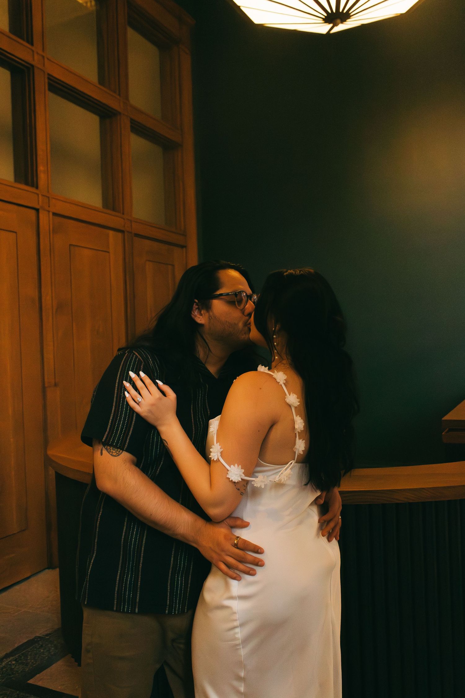 Intimate couple shares tender moments in warm lighting against a wood-paneled wall.