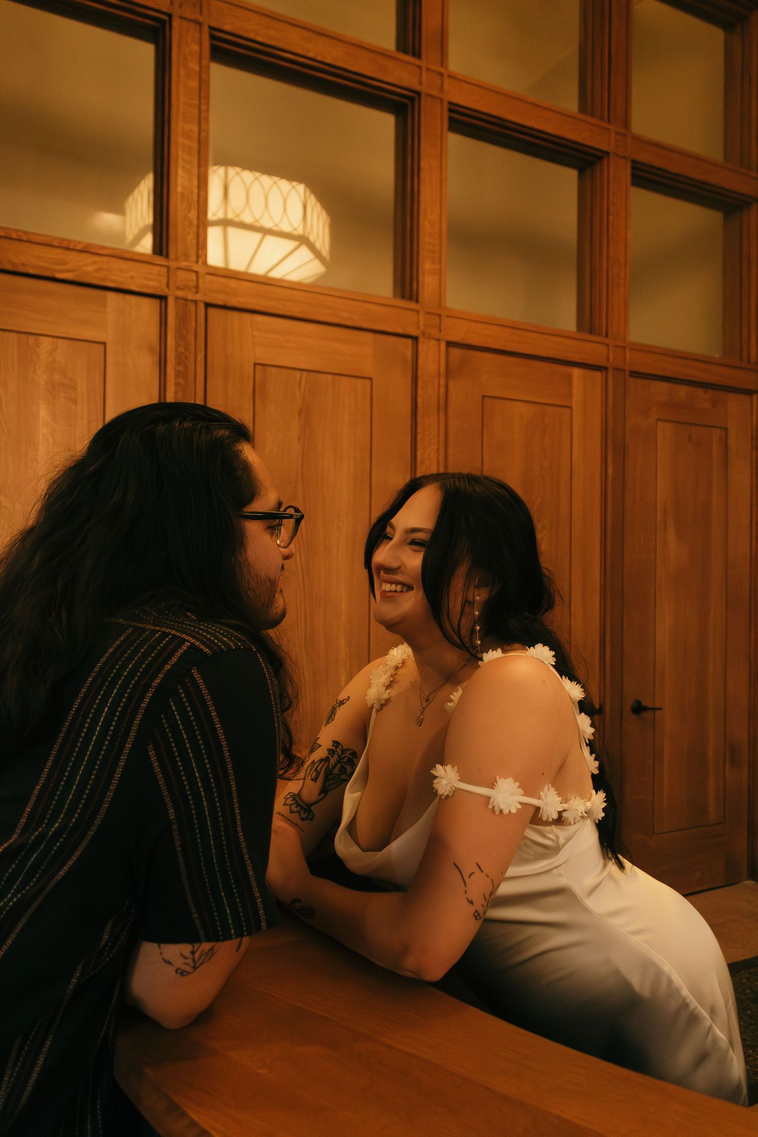 Couple sharing an intimate moment together on wooden benches in dimly lit hallway.