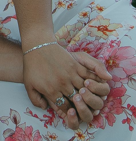 Hand wearing an engagement ring is seen against a pink floral watercolor background in a romantic wedding photo series.