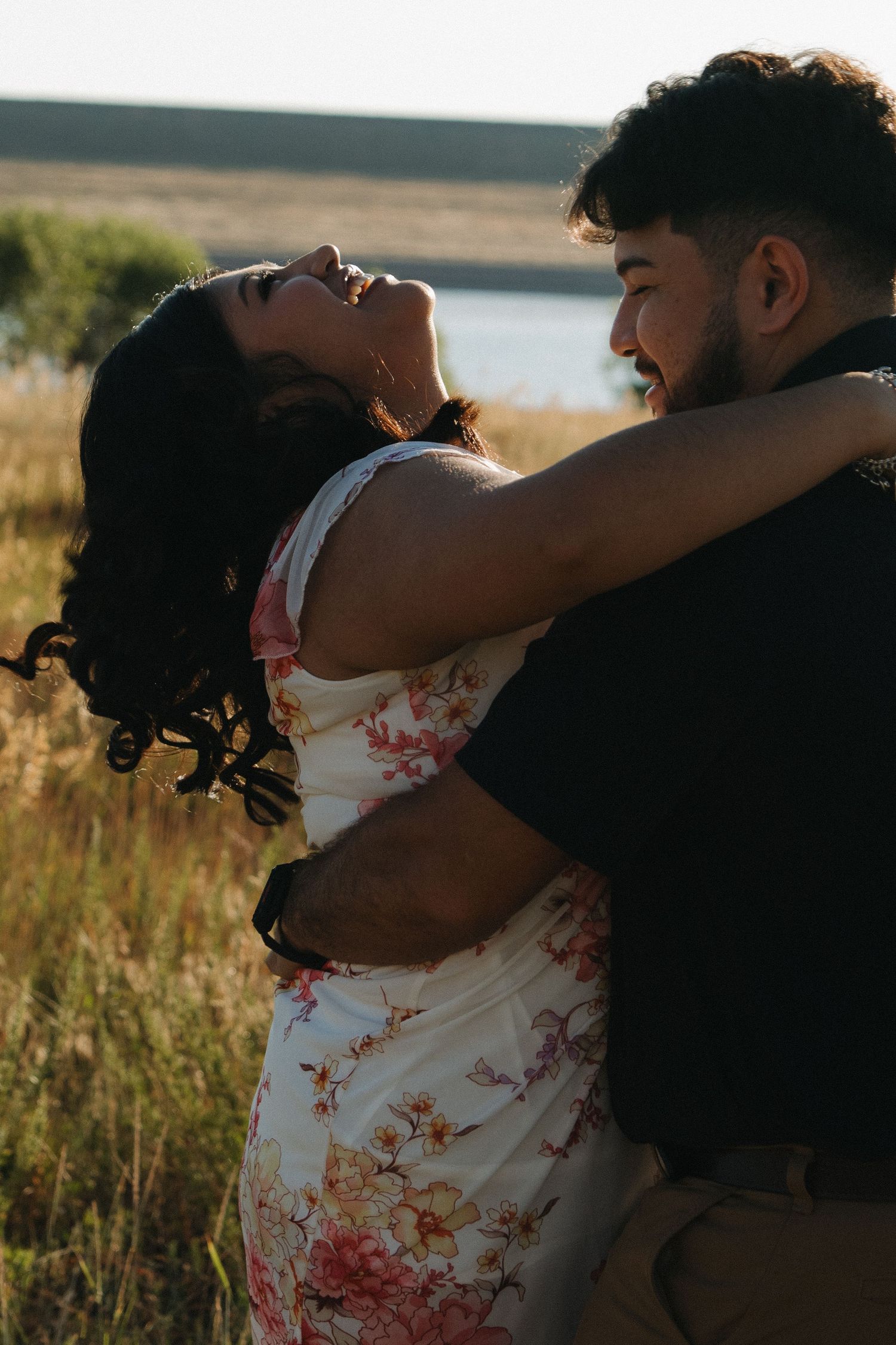 A couple shares a joyful embrace while dancing in a sunlit field.