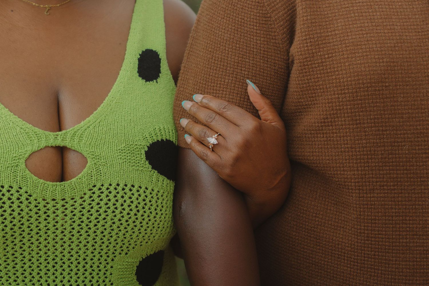 Close-up of hands wearing engagement ring against lime green and brown clothing.