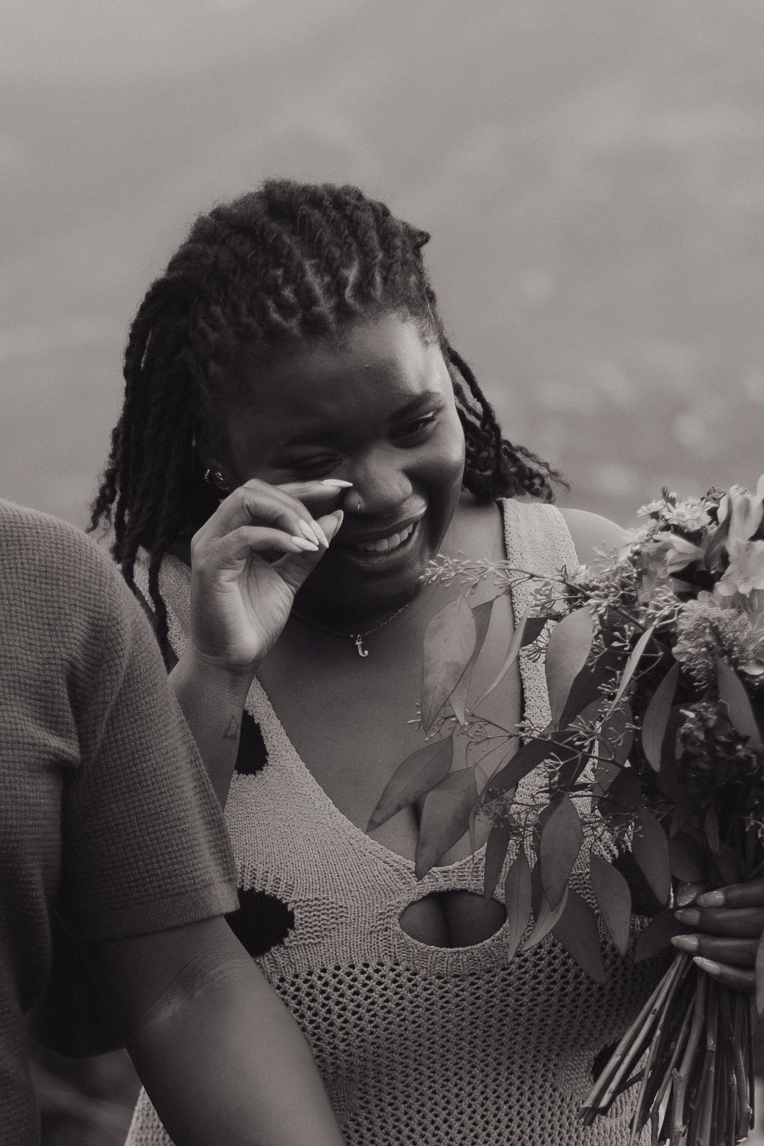 Person with braided hair and cozy sweater laughing while holding a floral bouquet in black and white photography.