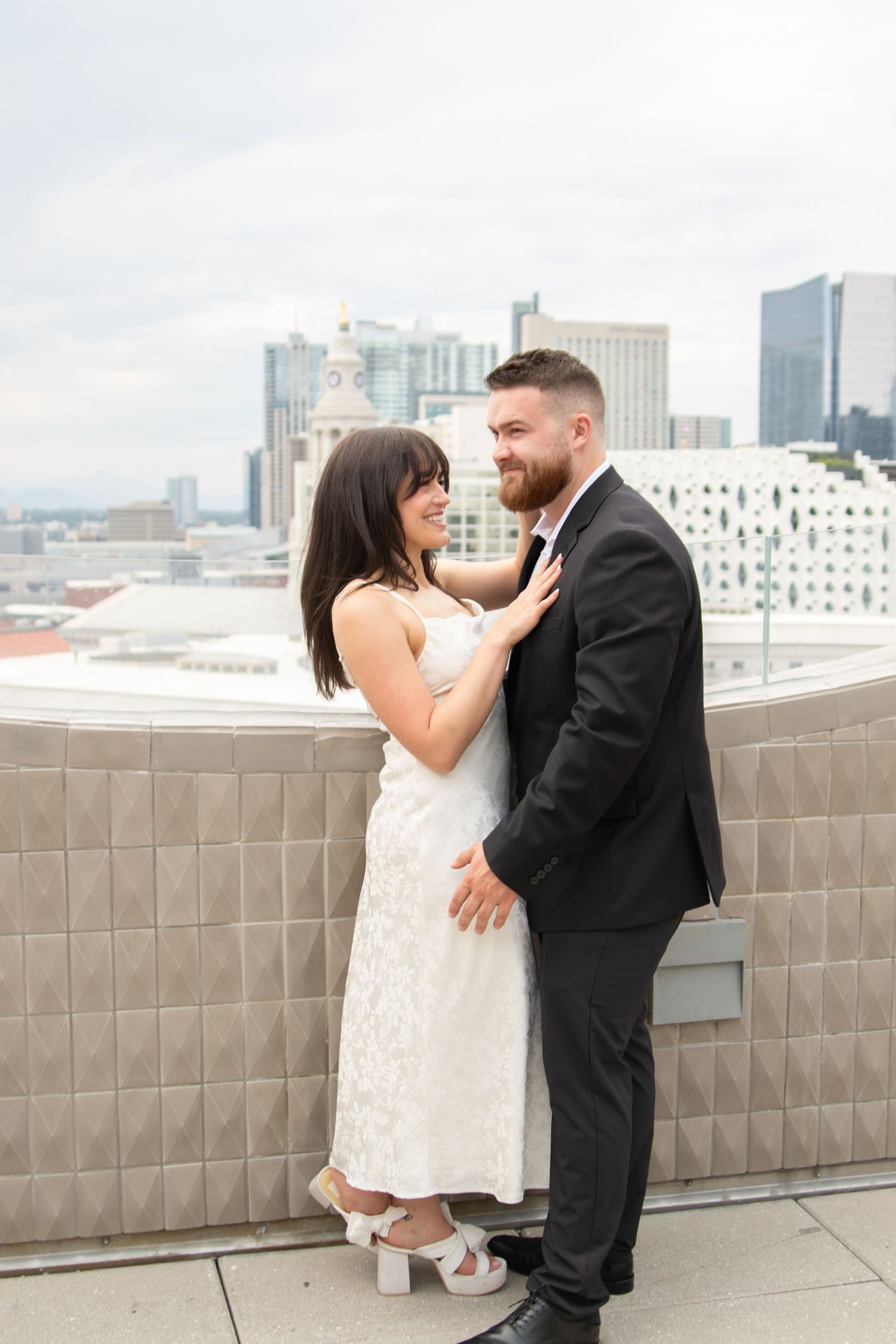 A happy wedding couple shares intimate moments on a rooftop terrace with city buildings visible in the background.
