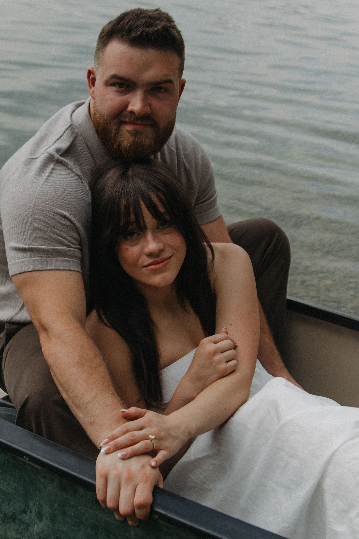 Couple cuddles affectionately along the edge of a boat on serene waters.