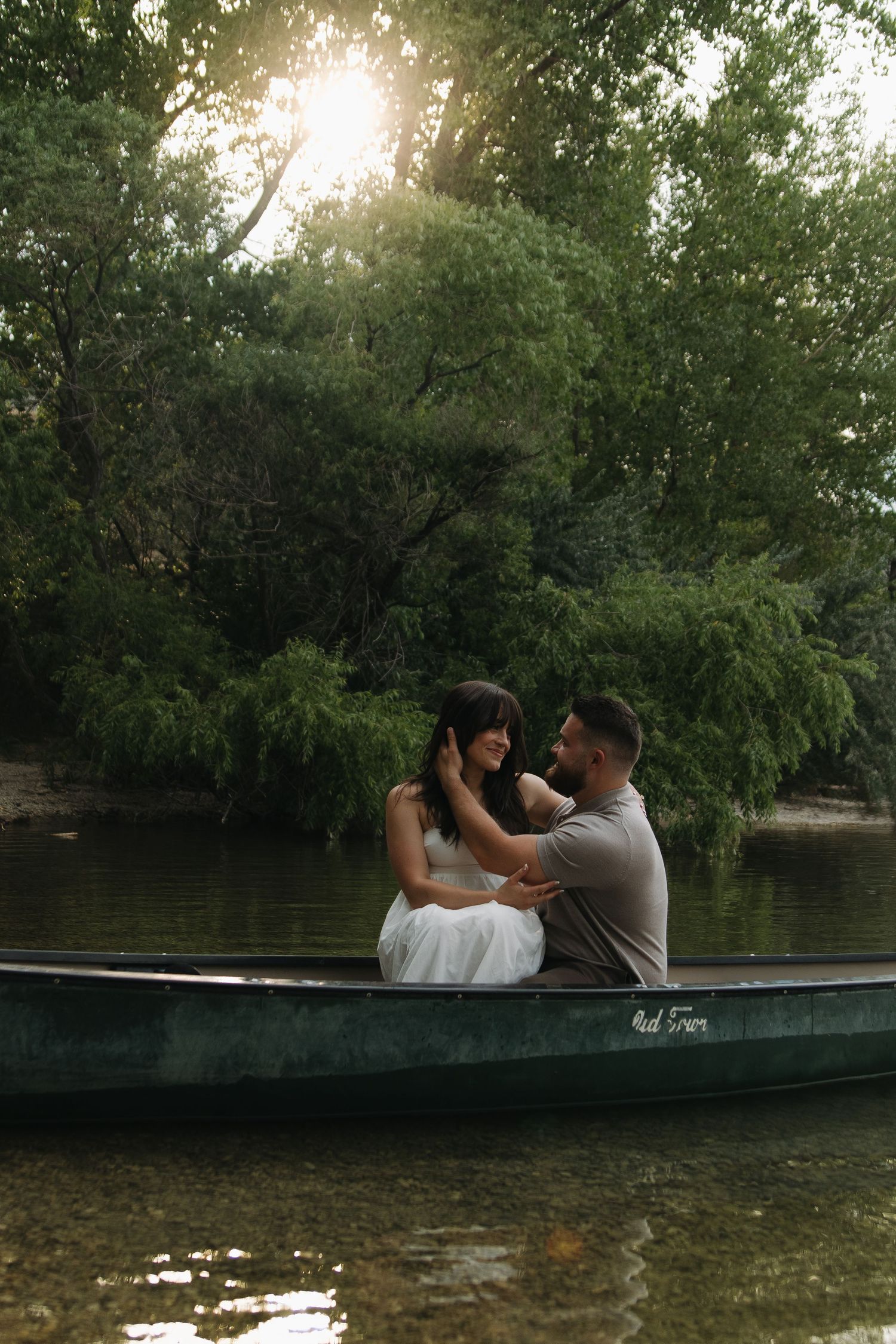 A romantic couple sitting together in a canoe on a tranquil lake surrounded by lush trees.
