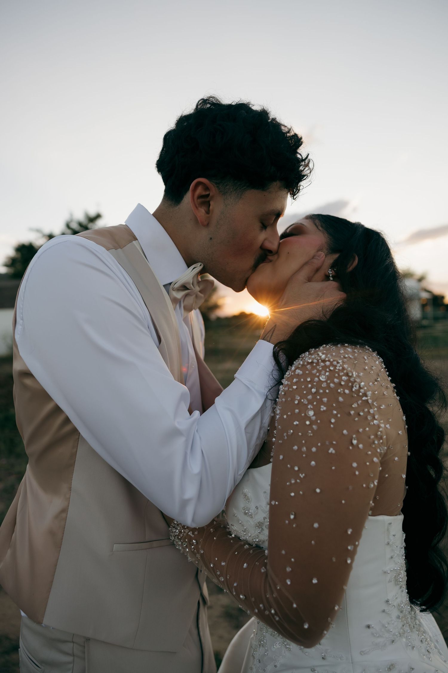 Bride and groom share a romantic sunset kiss, bride wearing pearl-embellished wedding gown.