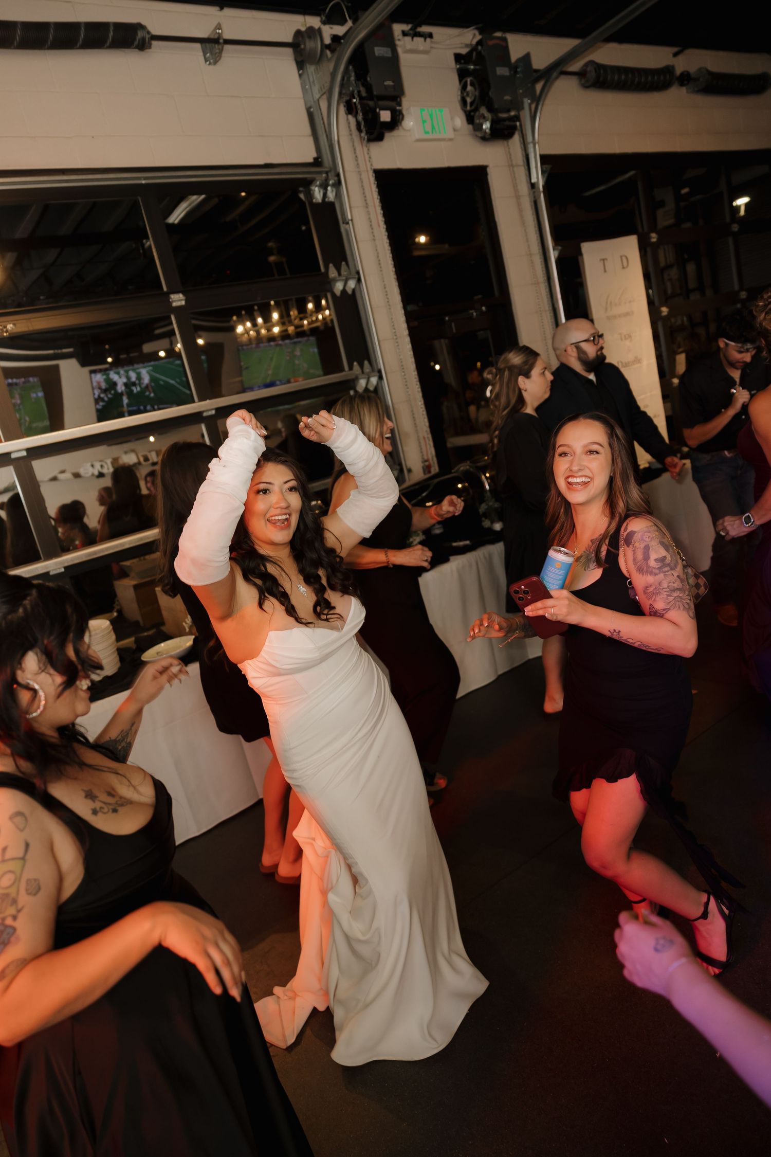 Bride in white gown dancing joyfully with guests at lively indoor wedding reception party.