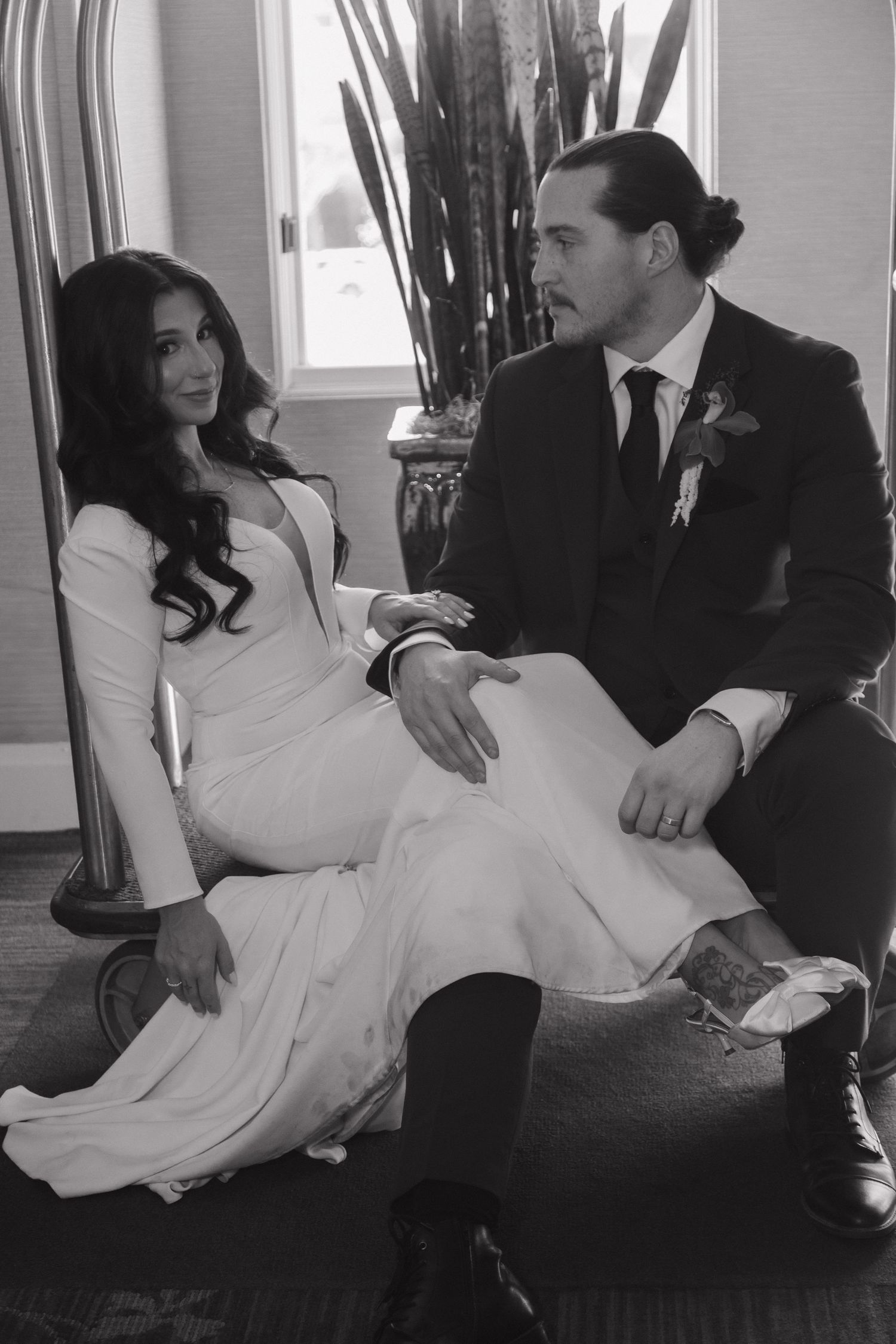 Black and white portrait of bride in white gown and groom in dark suit seated together.