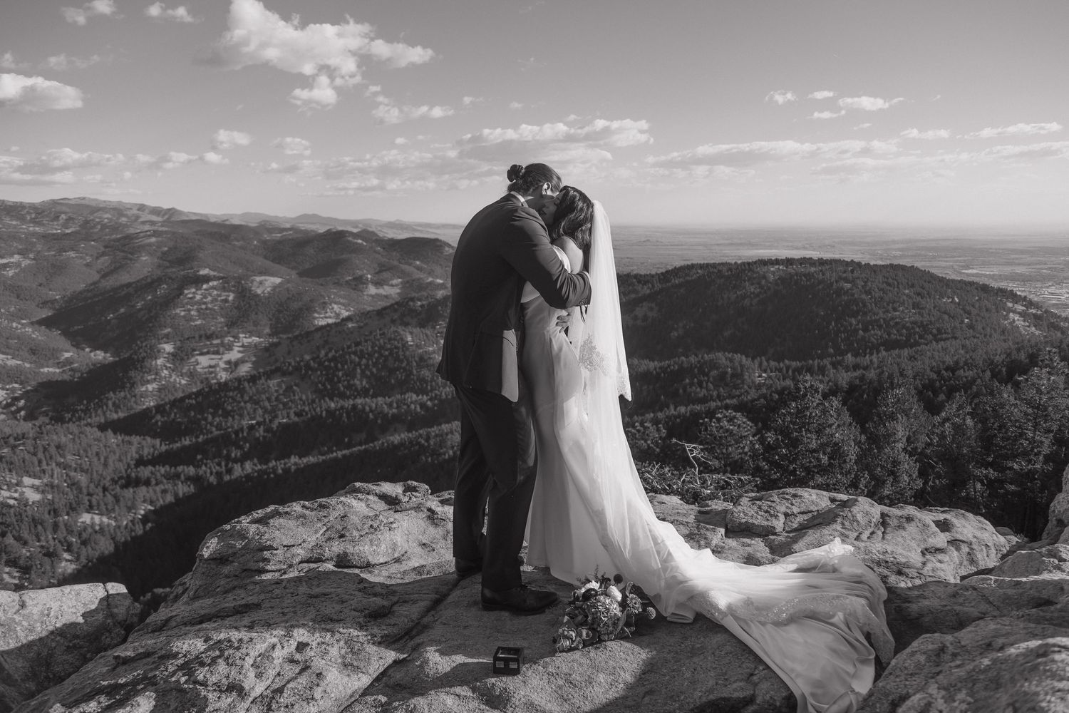 Newlyweds share first kiss on stunning mountain summit with breathtaking Colorado landscape below.