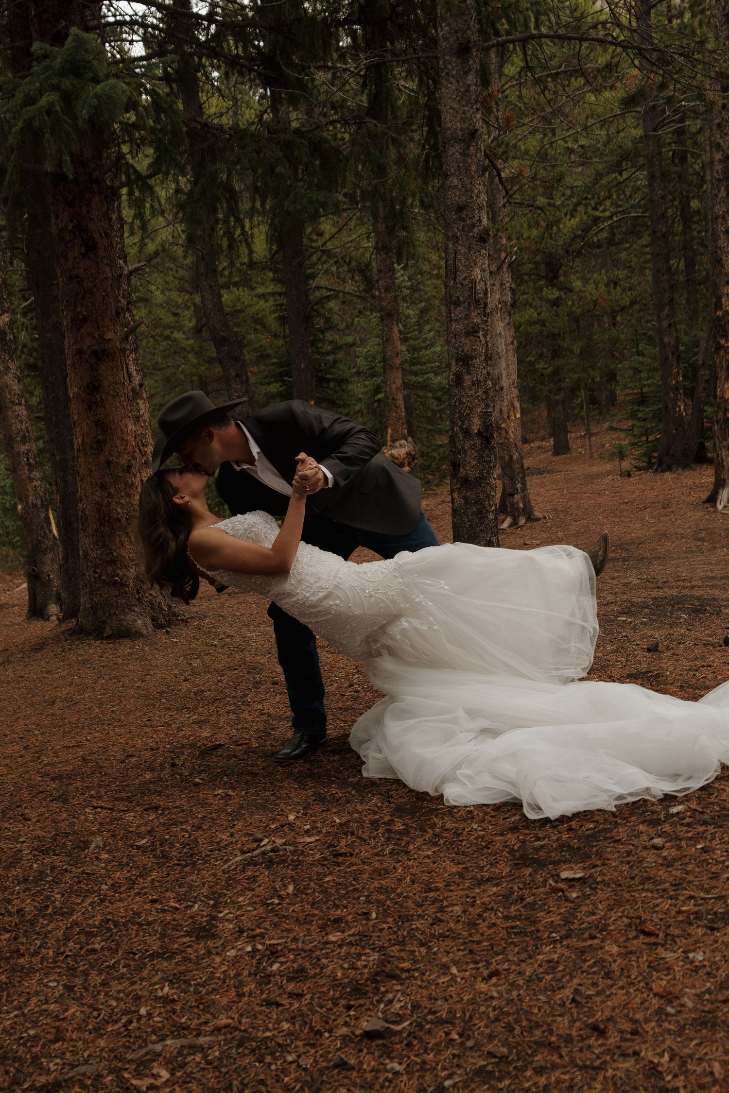 Dramatic dip pose in a forest setting with pine needles covering the ground.
