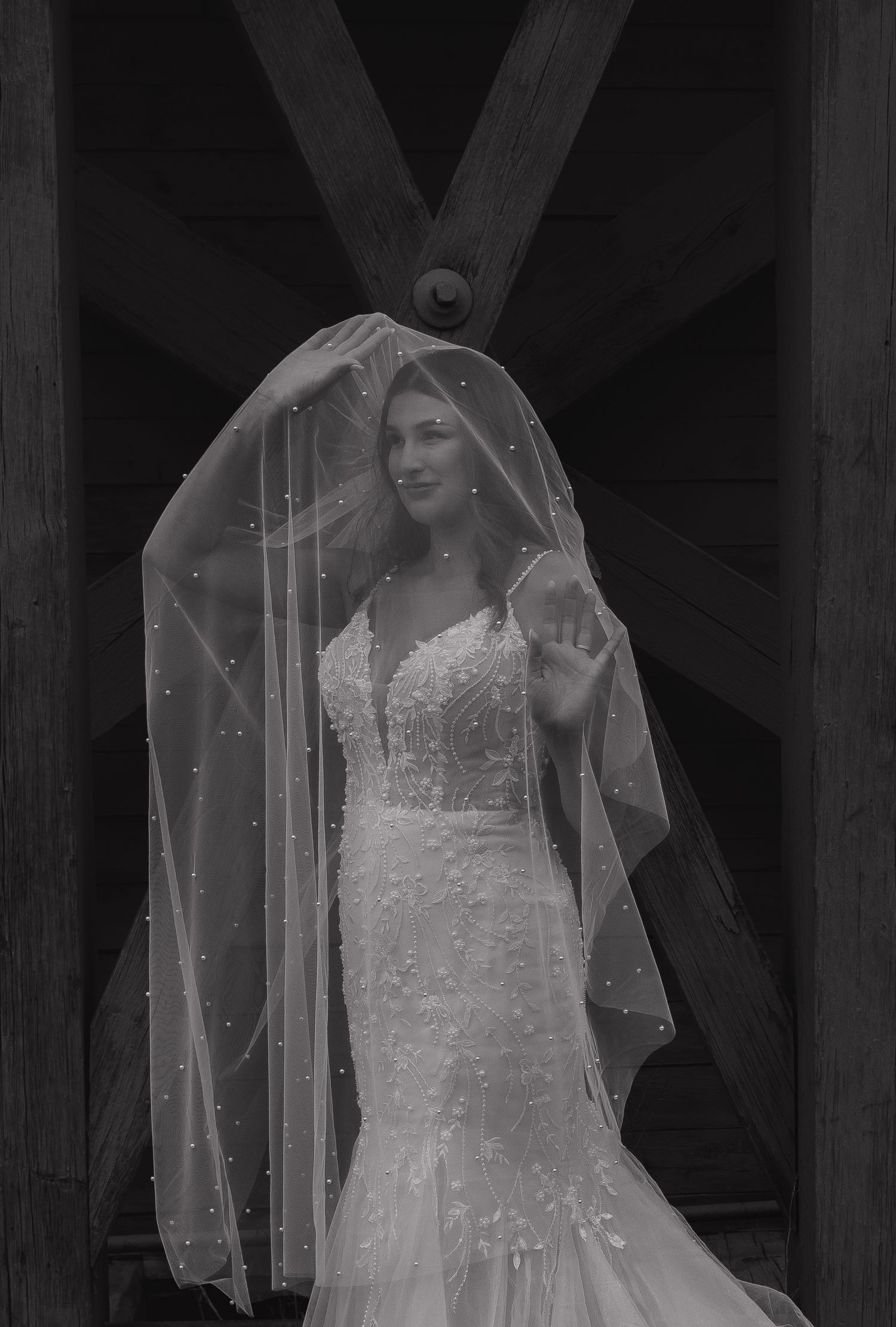 A wedding dress with delicate lace details hangs elegantly in a rustic wooden setting.