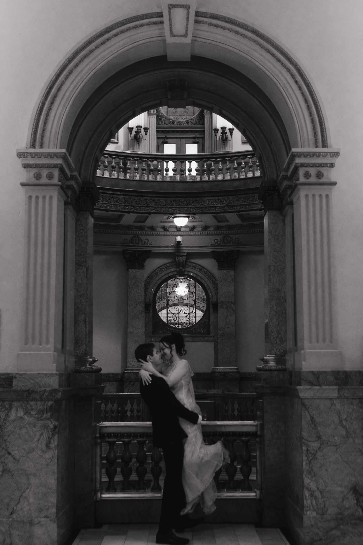 Romantic moment under grand arched hallway with classical architecture.