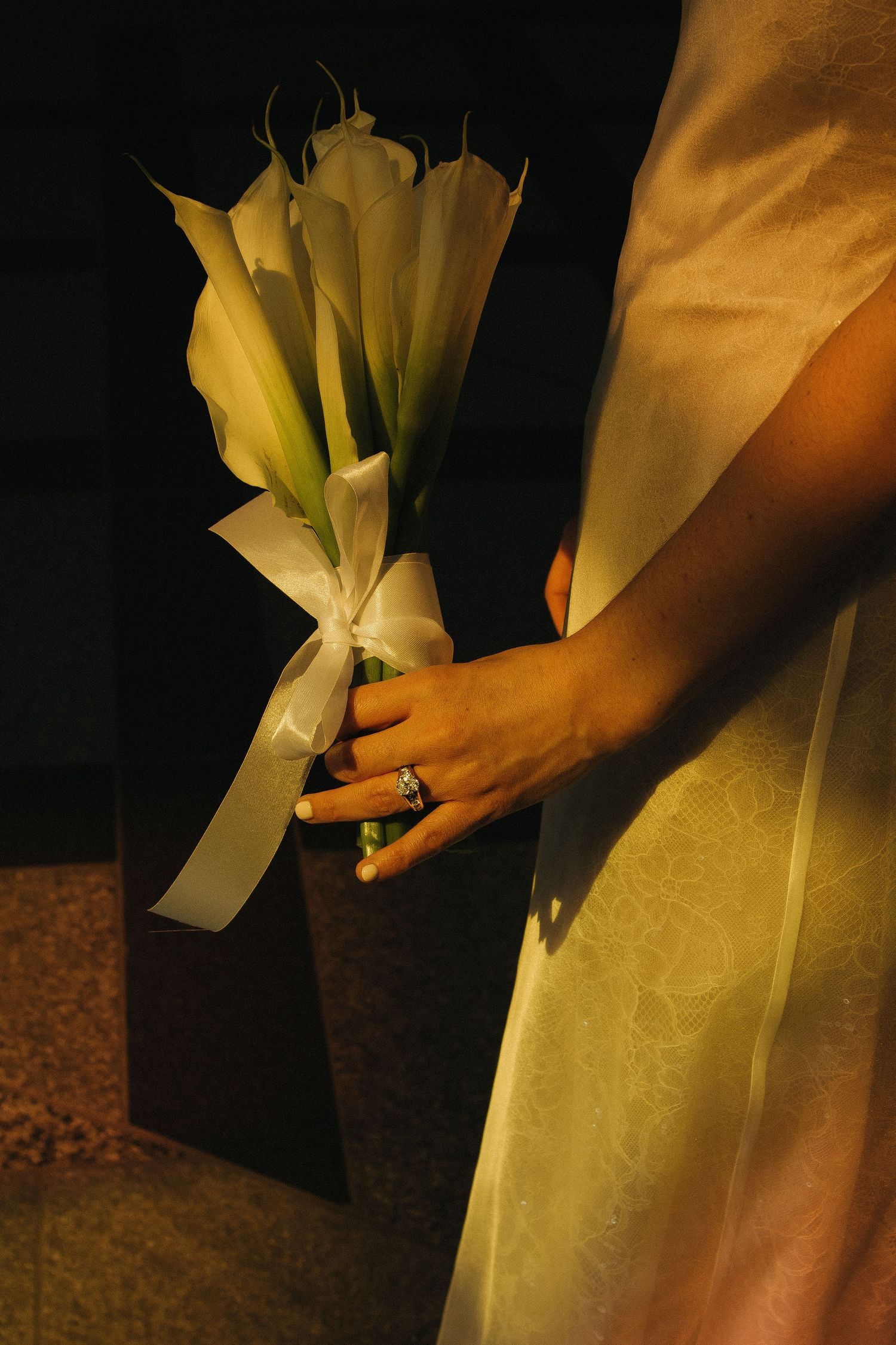 Close-up of wedding bouquet with white calla lilies against formal attire.
