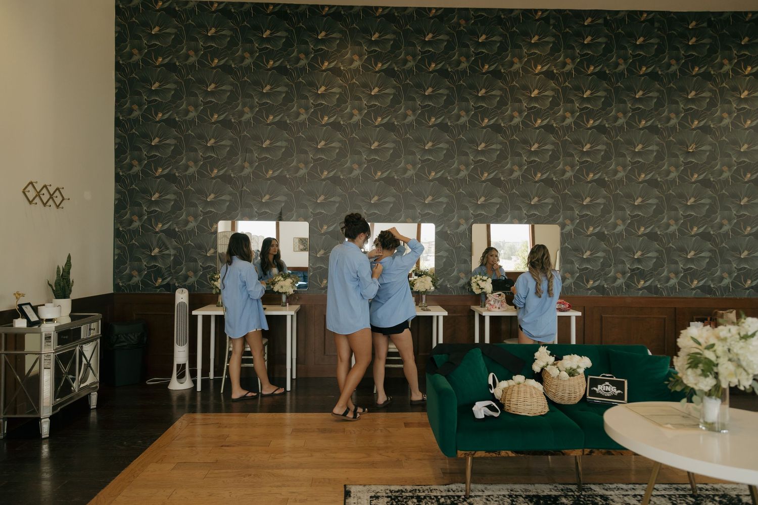 Bridesmaids in matching blue robes getting ready together at vanity mirrors in a stylish wedding suite.