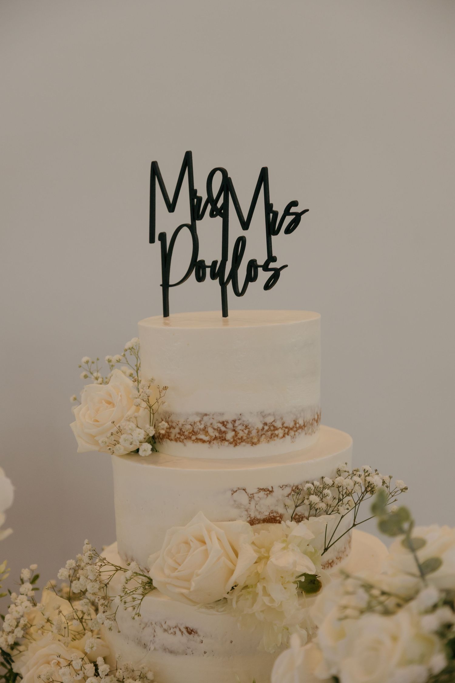Elegant two-tier white wedding cake with Mr and Mrs Poulos topper and white floral decorations.