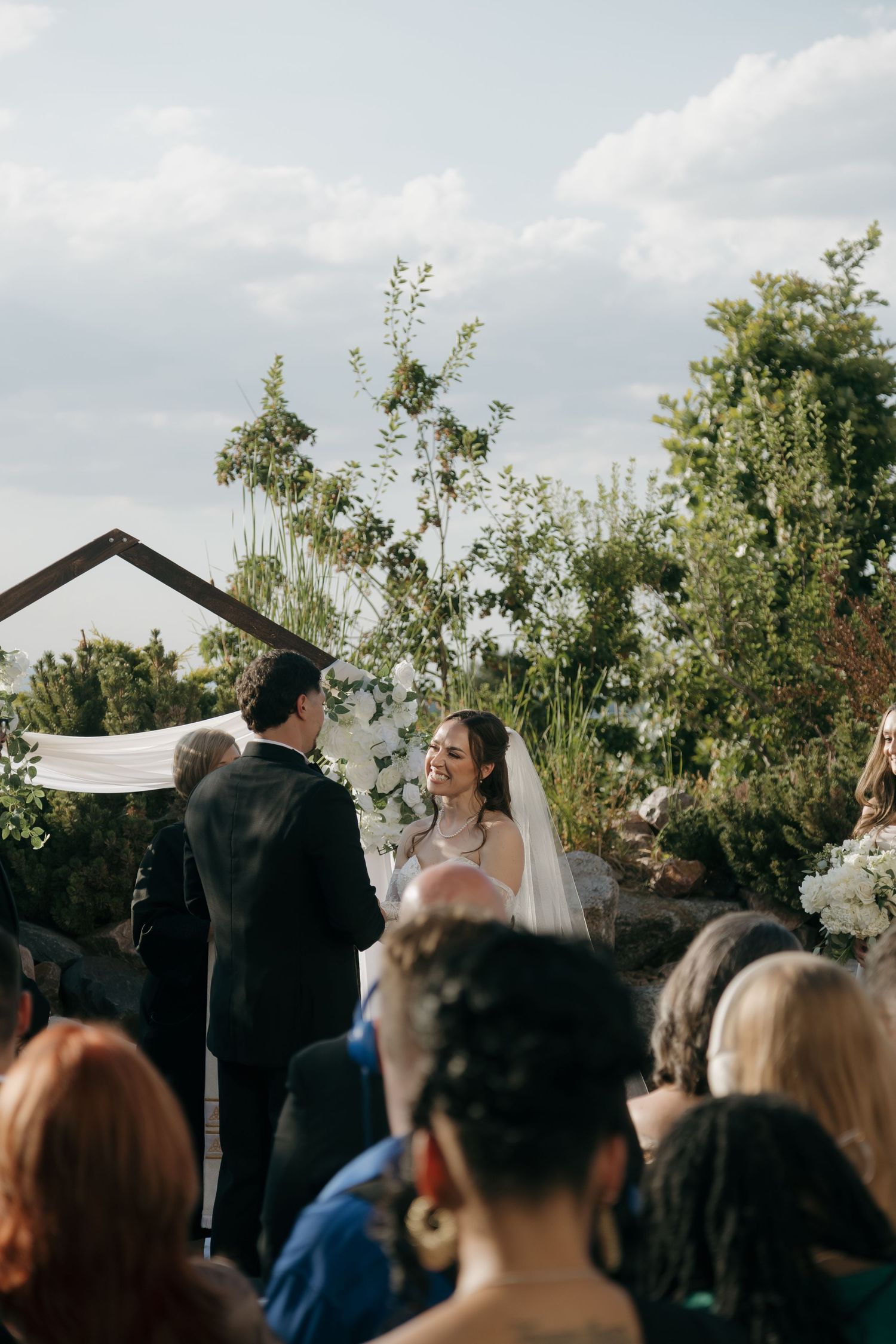 Bride and groom exchange vows at an outdoor wedding ceremony with a wooden arch backdrop.