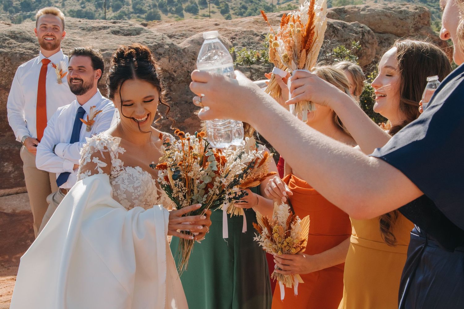 Bridal party celebrates outdoors with colorful dresses against mountain scenery.