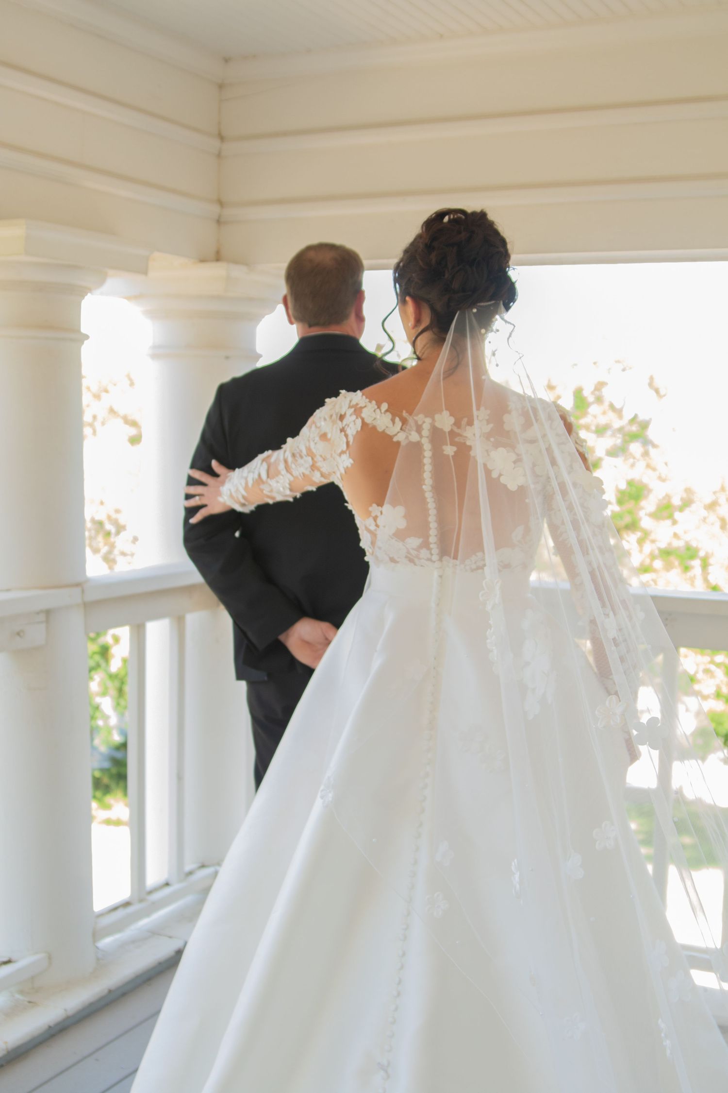First look wedding moment captured on a white porch with delicate lace details on the bridal gown.