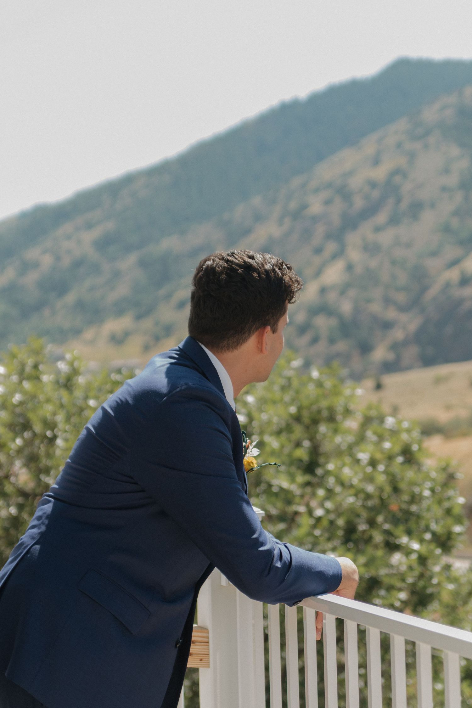 Person in navy blue suit looking over white railing with mountains in background.