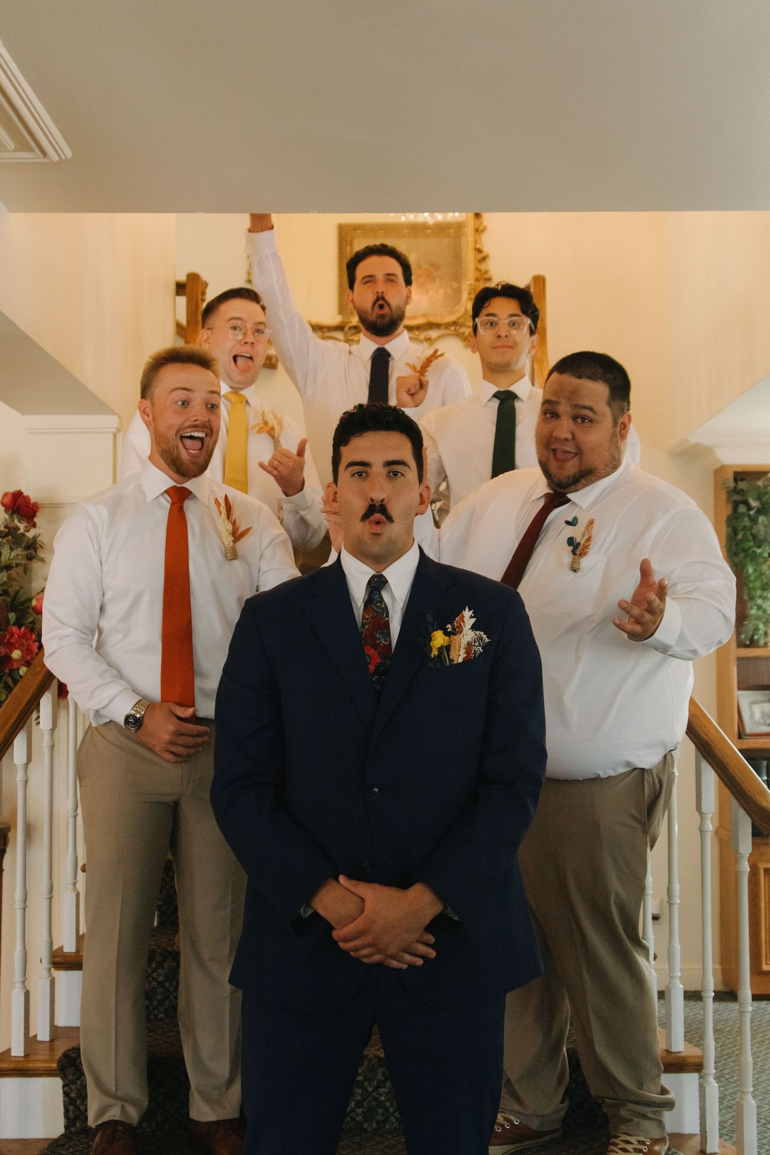 Wedding party gathering indoors wearing formal attire and colorful ties.
