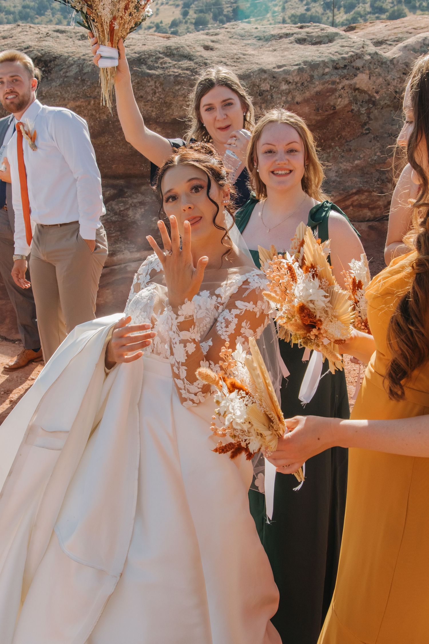 Wedding party celebrates with confetti toss against desert rock formations.