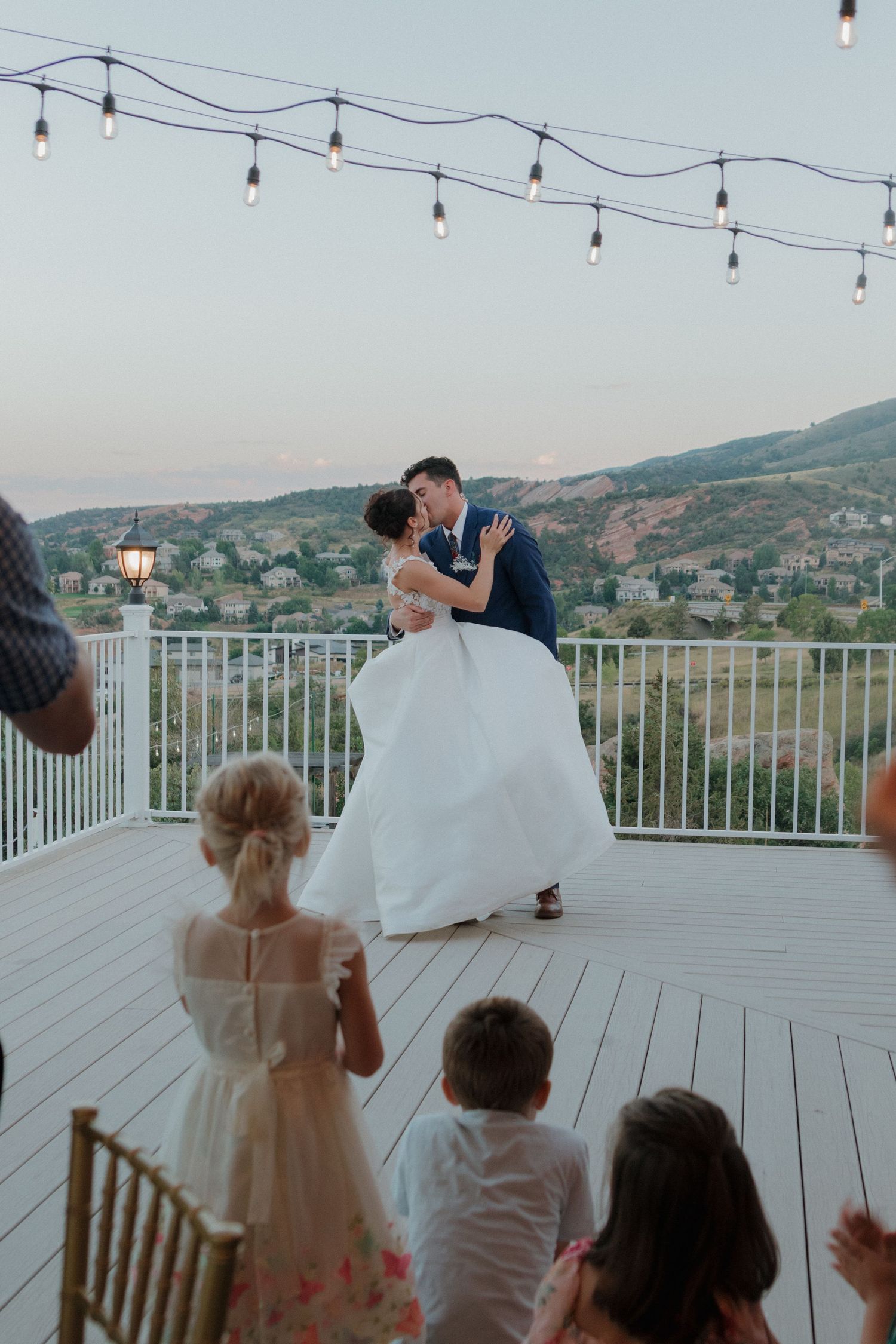 Wedding celebration on an outdoor deck with string lights and mountain views.
