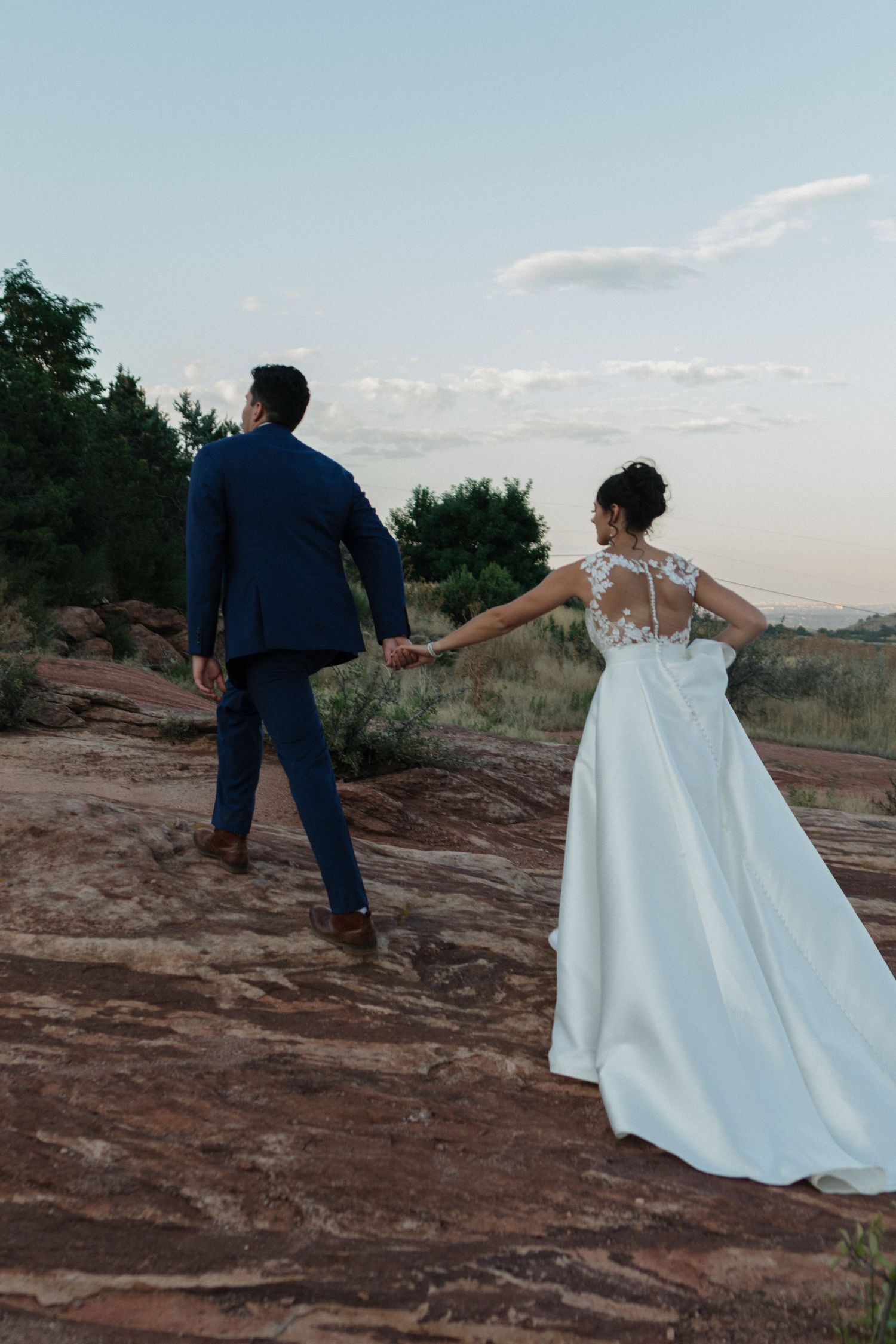 Bride and groom playfully walking and posing on red rock formations during sunset photo session.
