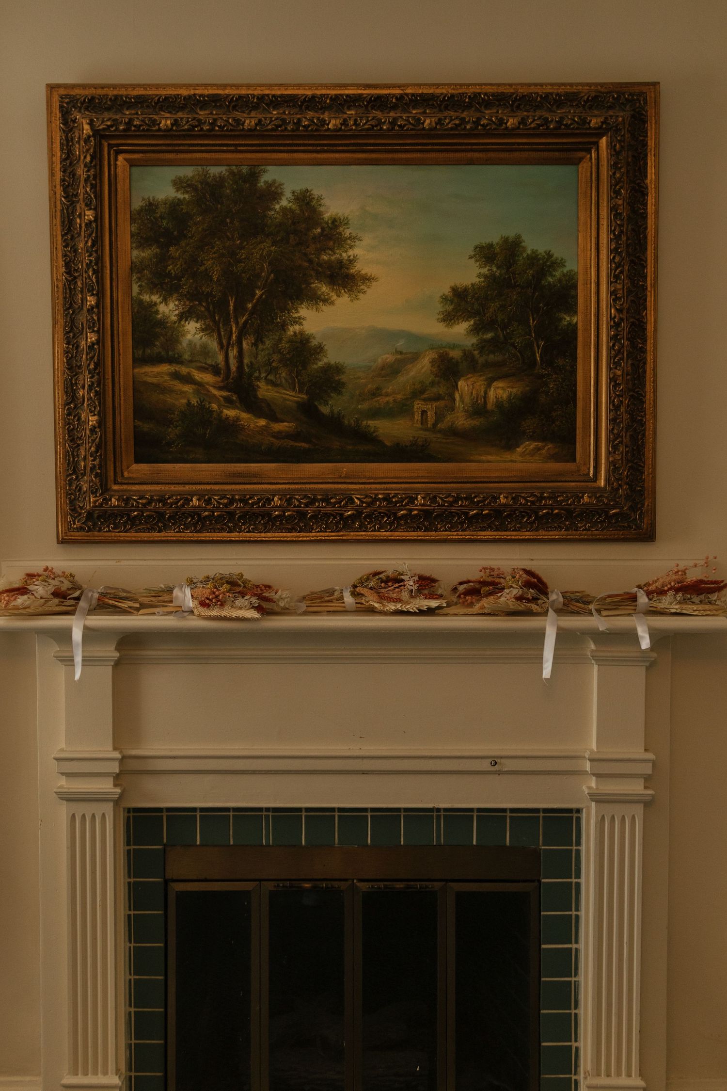 Elegant gold-framed landscape paintings hang above a fireplace with green tile and white trim.