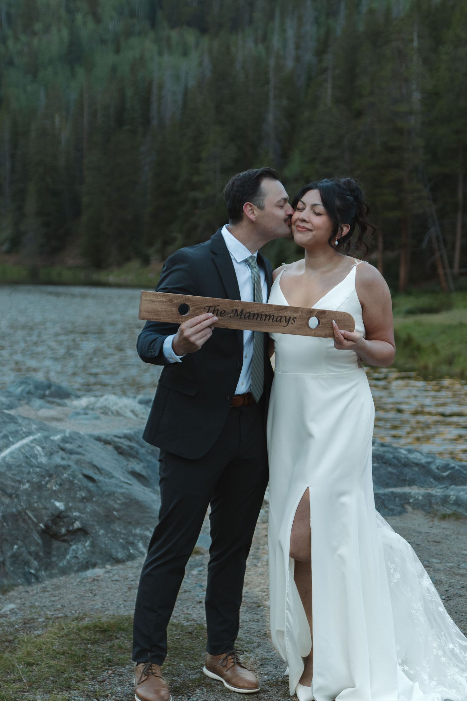 Wedding couple shares a romantic moment in their formal attire against a scenic outdoor backdrop.