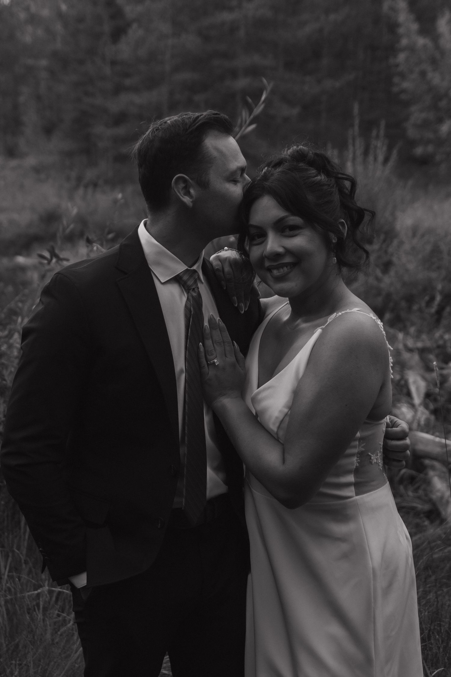 Black and white photo captures intimate moments between newlyweds in a forest setting.