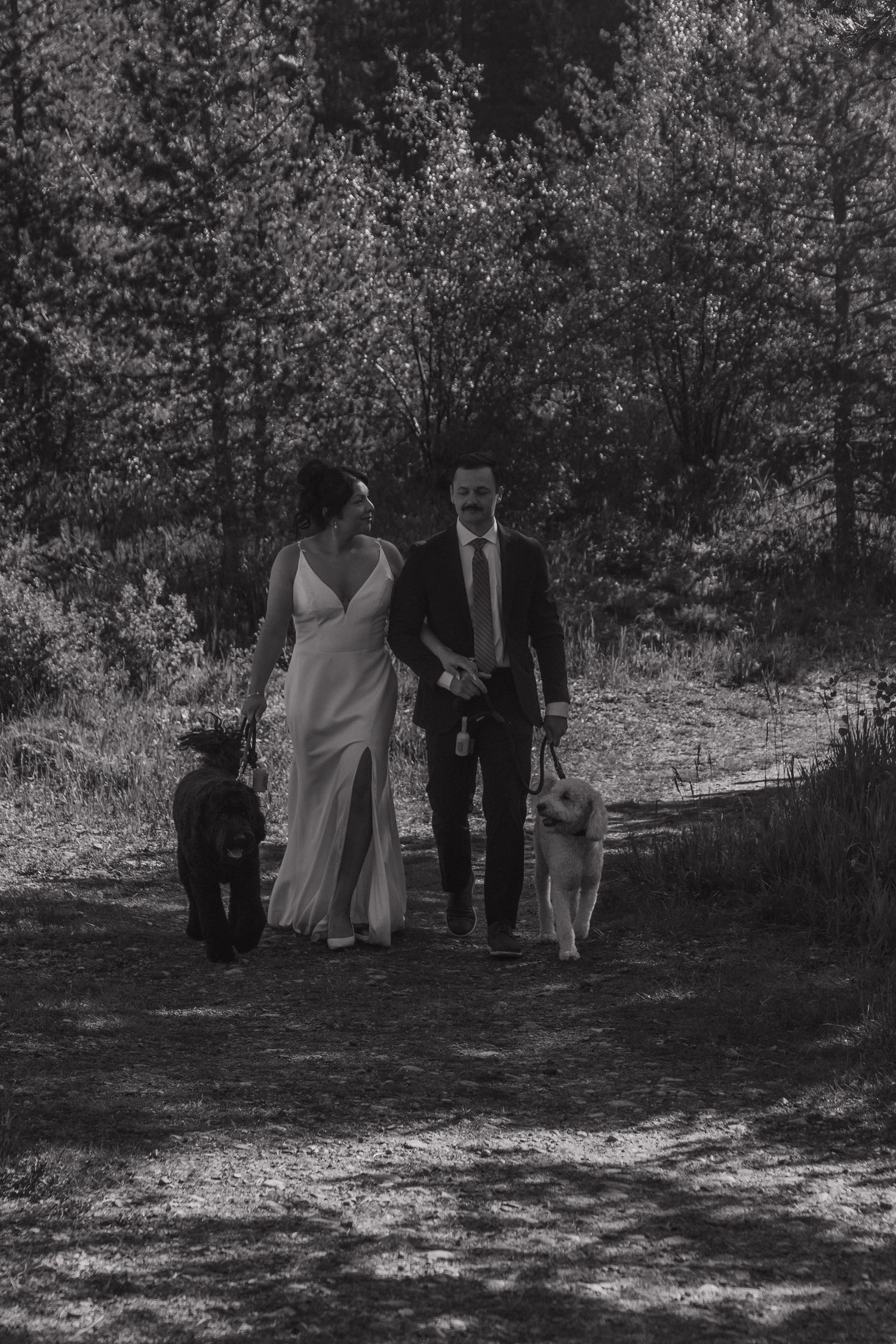A black and white photo of a wedding party walking through a wooded area.