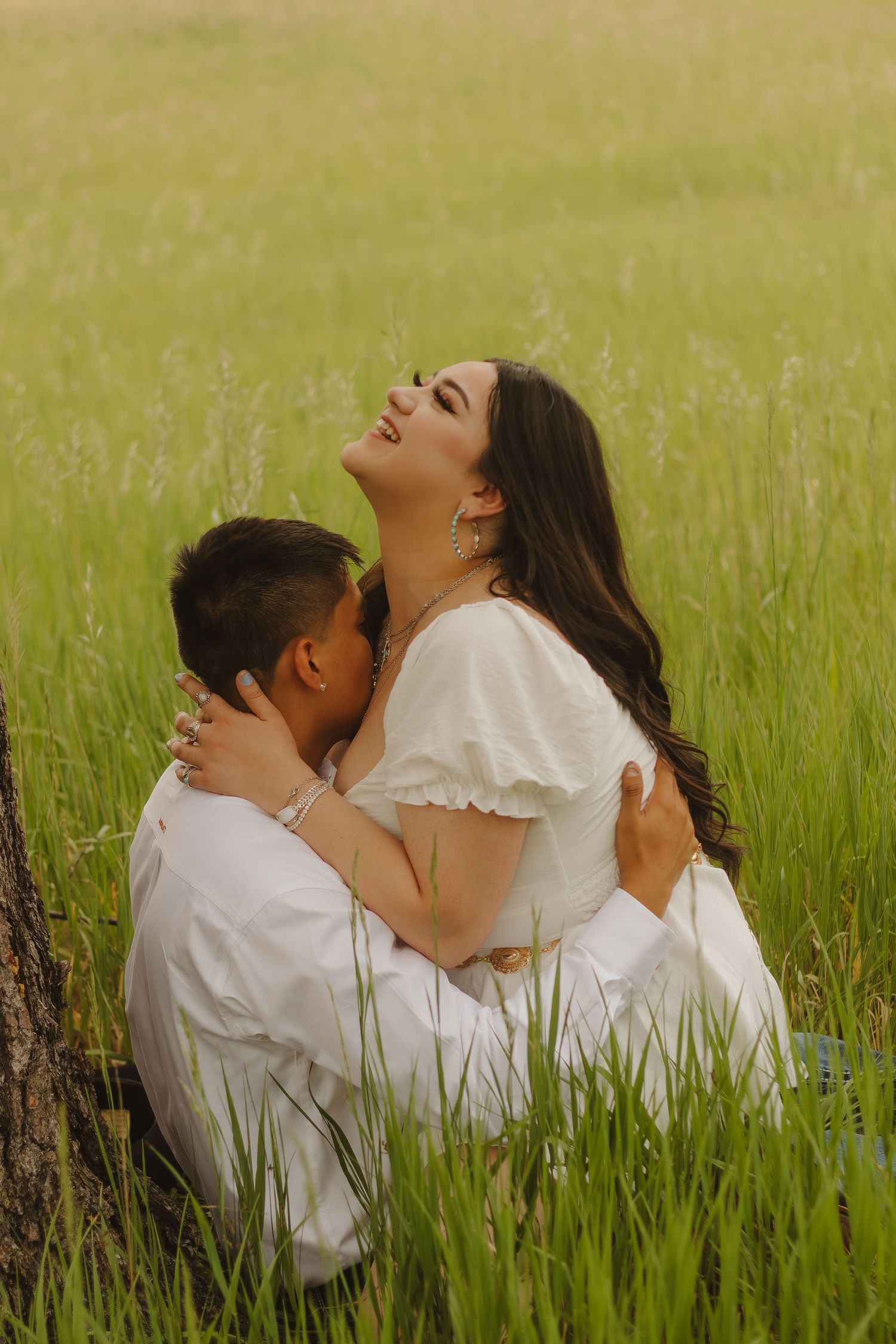 Candid shot of a couple embracing joyfully in tall grass during sunset.