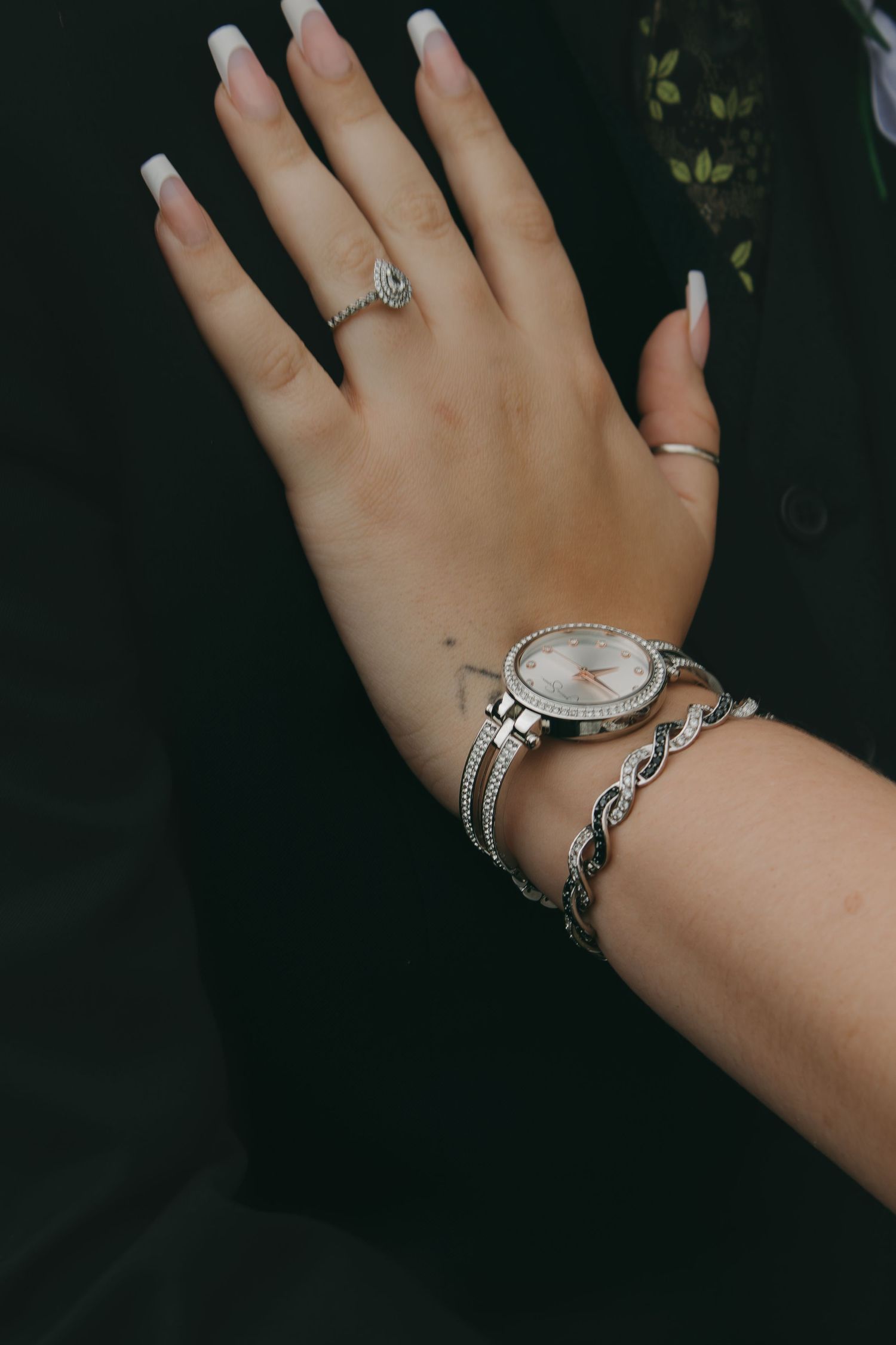 Woman's hand showing elegant jewelry including rings and bracelet against dark background.
