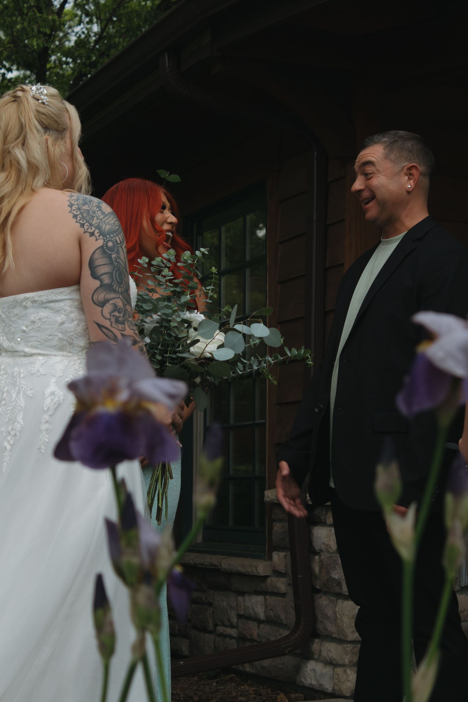A bride in a detailed white dress stands outdoors near a rustic stone building.