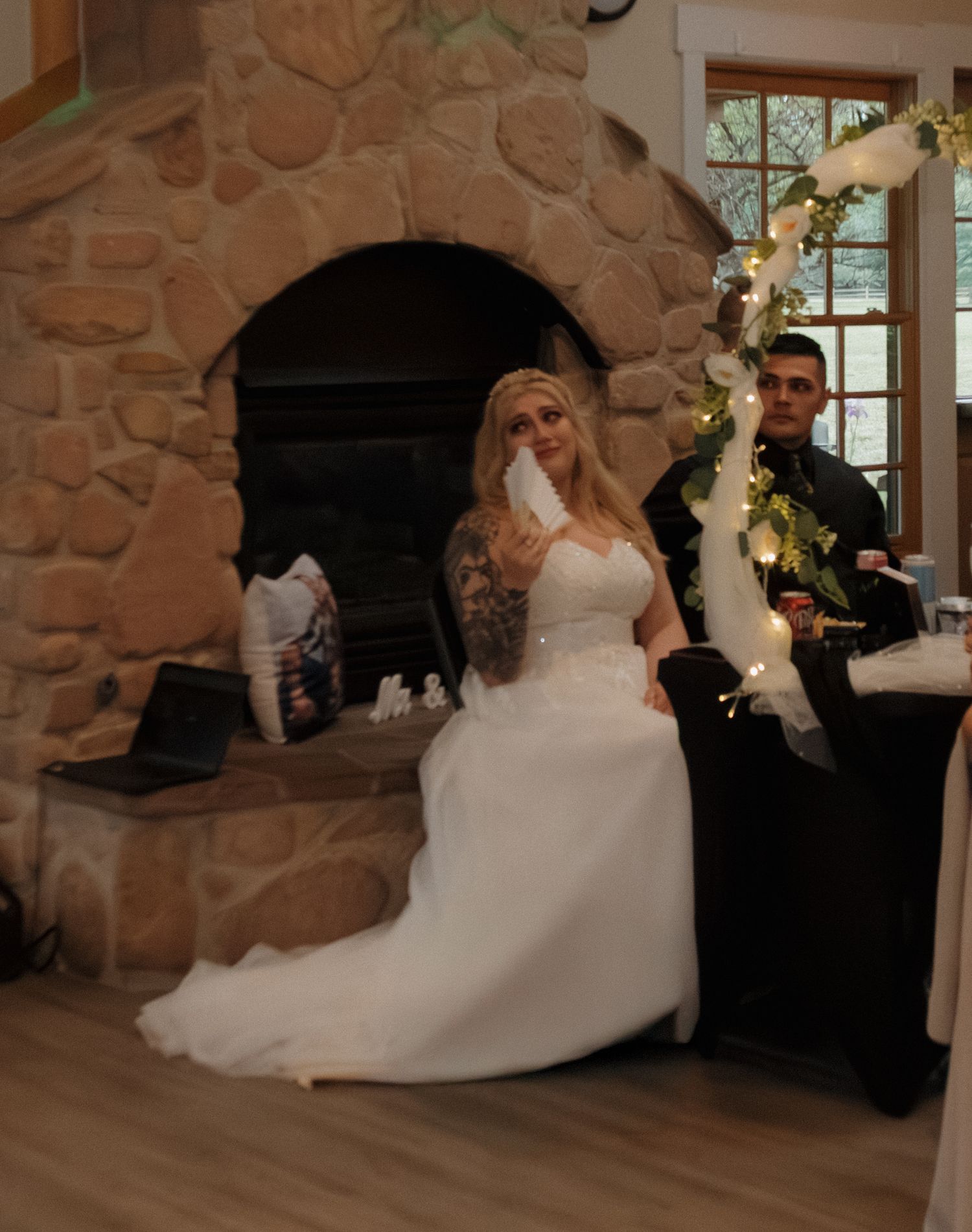 Elegant wedding reception setup with decorated arch and stone fireplace in rustic indoor venue.